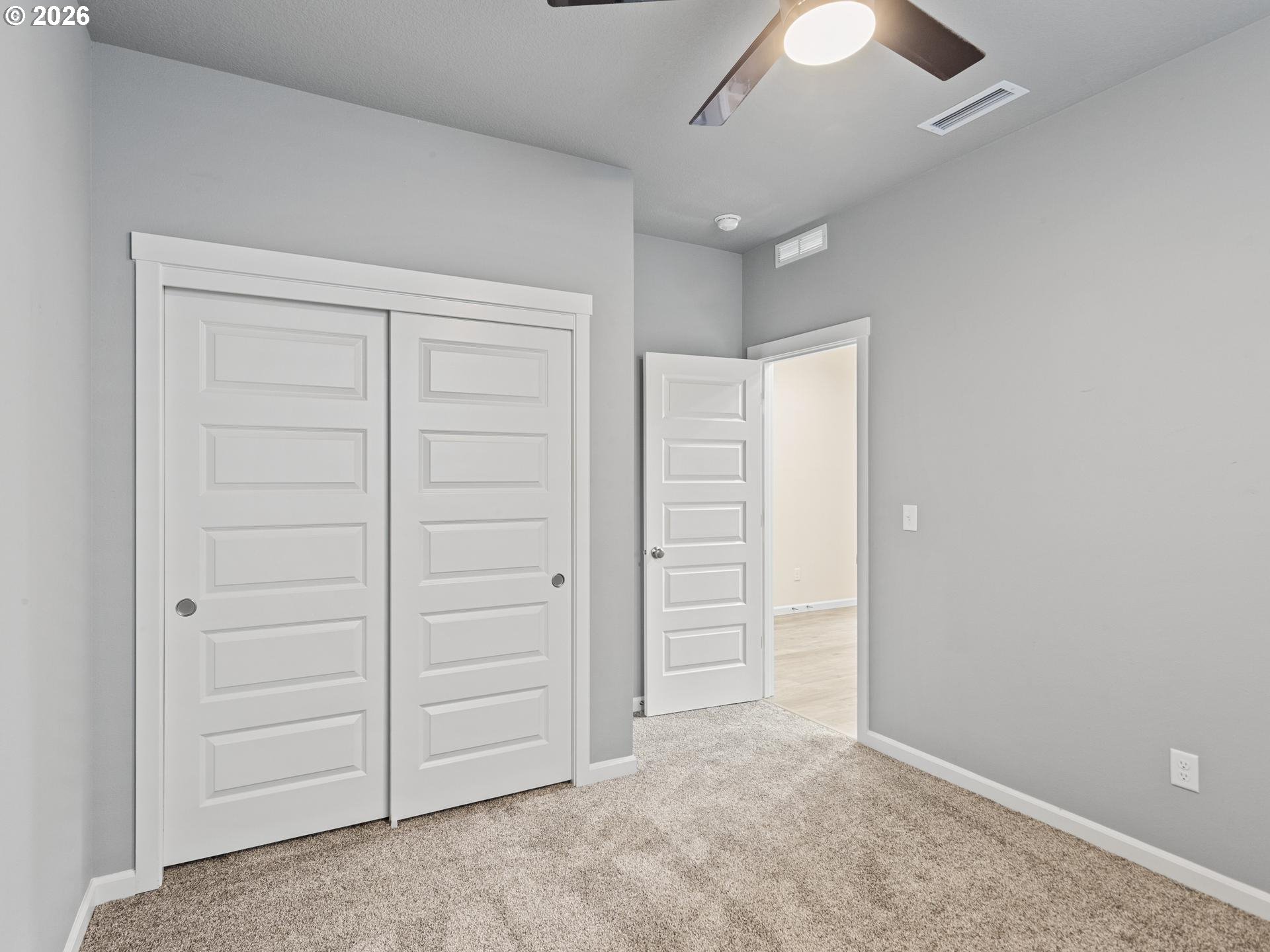 Empty carpeted room with large white paneled closet doors and an open doorway.