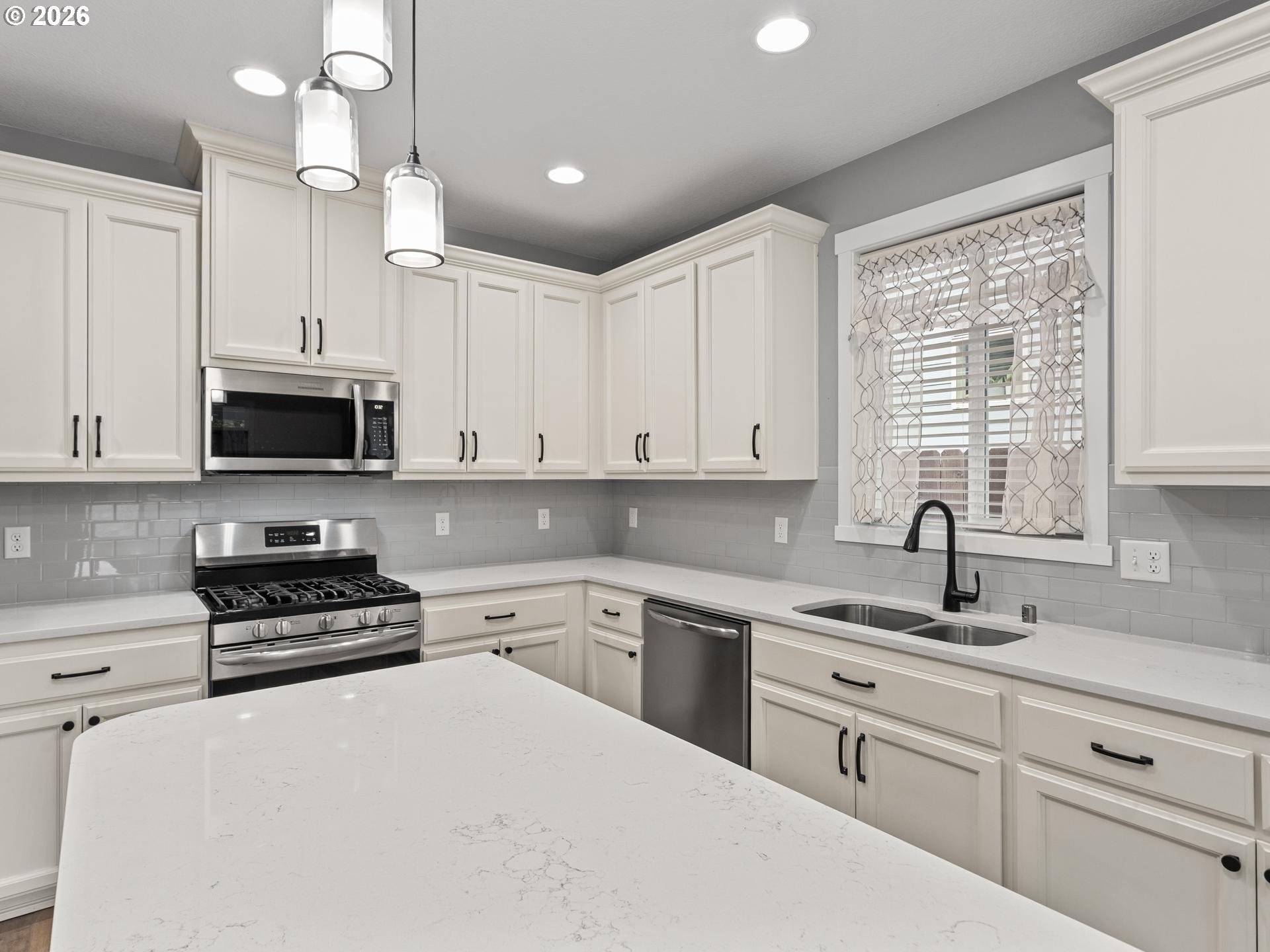 Kitchen with white cabinets, a large quartz island, stainless appliances, and a gas range.