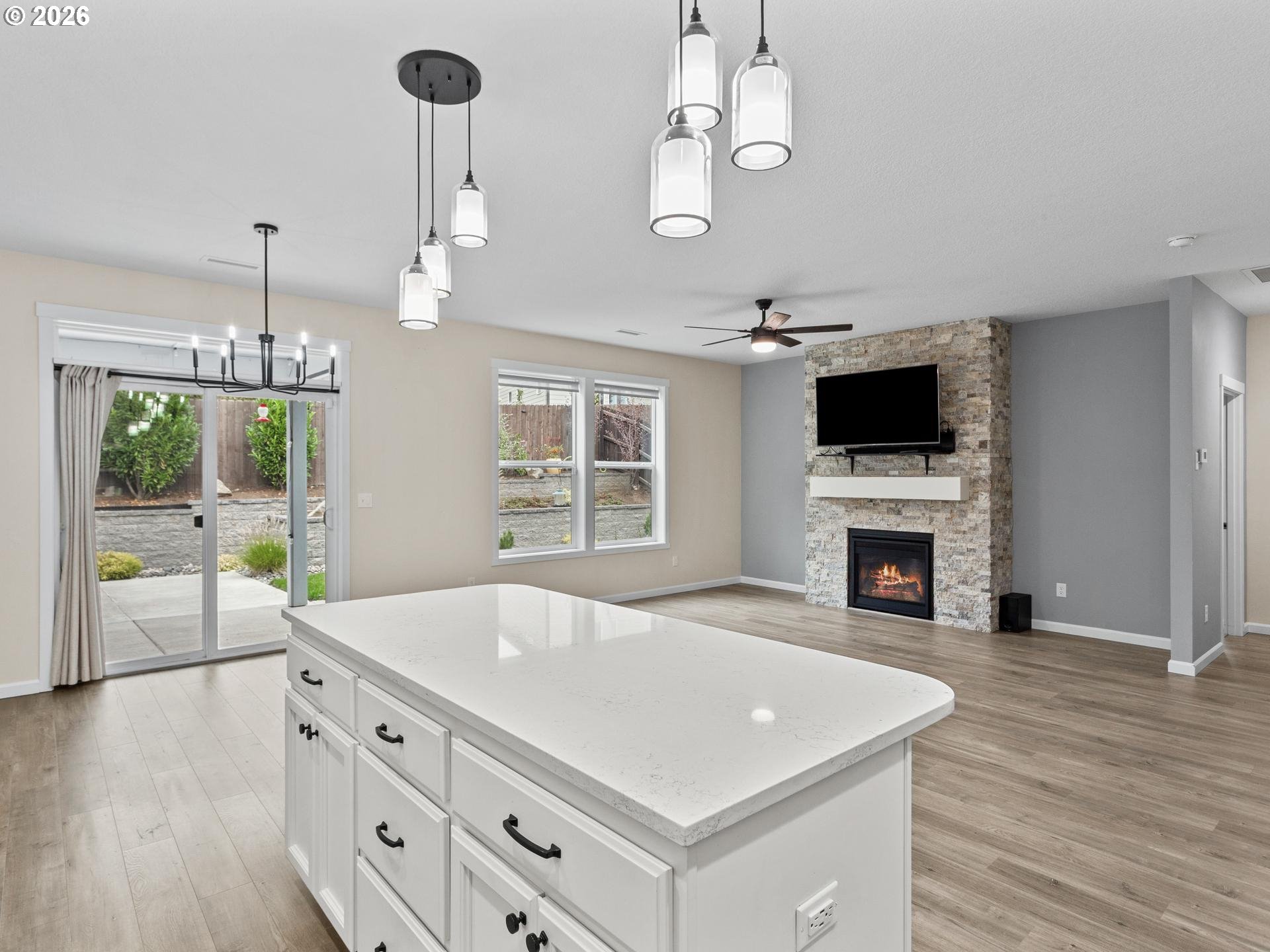 Open-plan kitchen and living room with a large white island and stone fireplace.