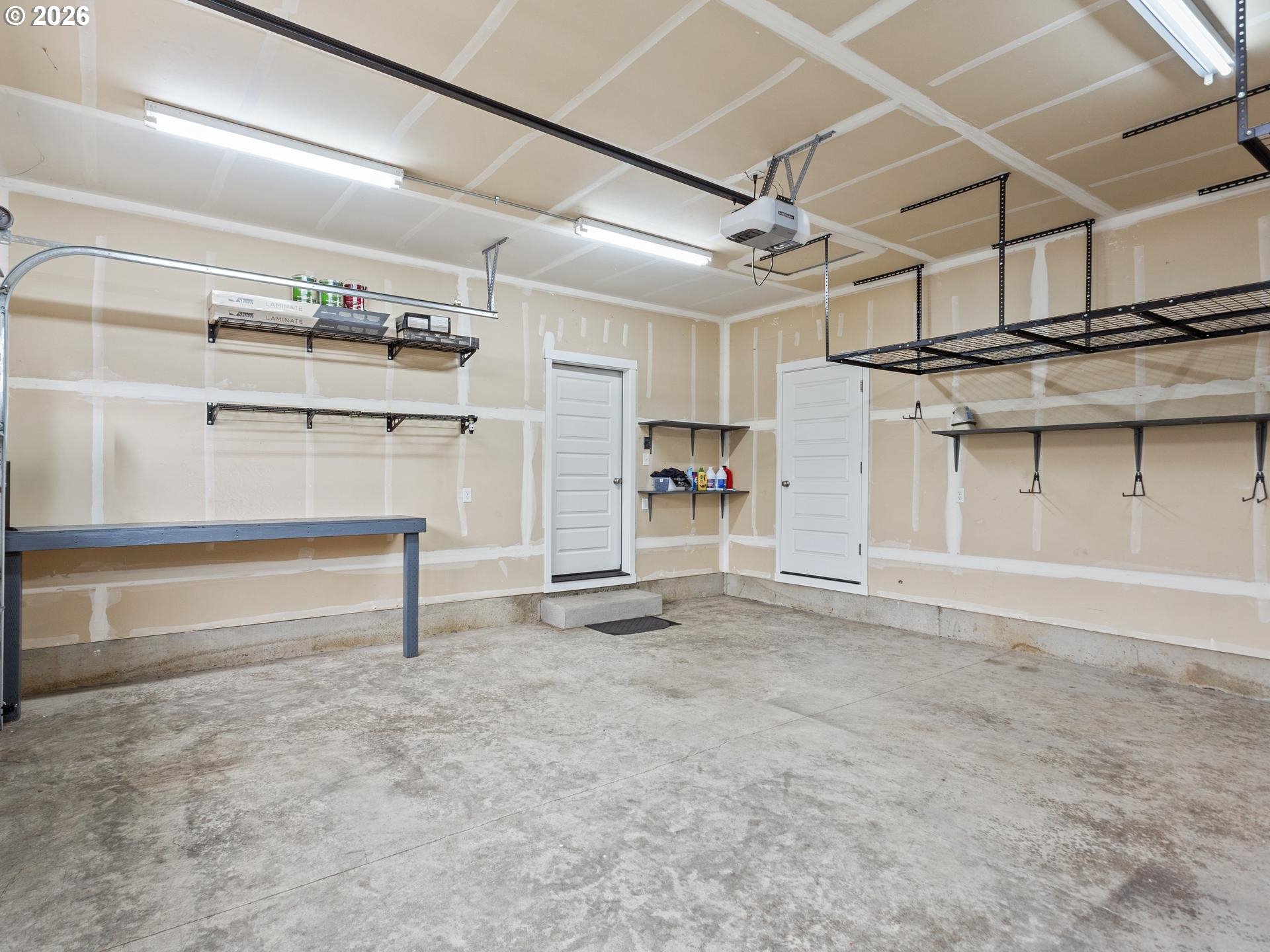 Spacious garage with overhead storage racks, wall shelving, a workbench, and concrete flooring.