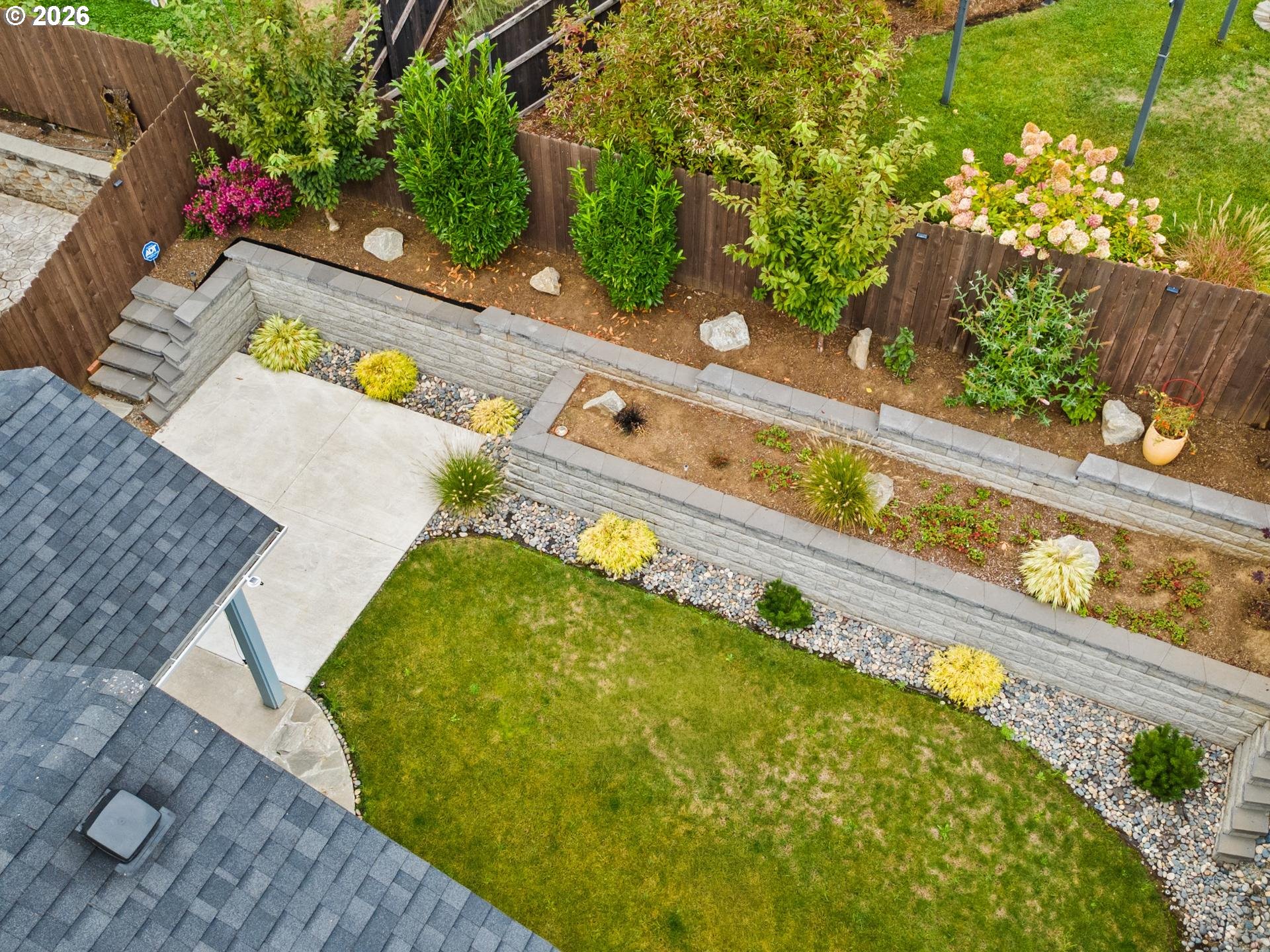 Landscaped backyard with curved stone retaining walls, a lawn, patio, and flowering shrubs.