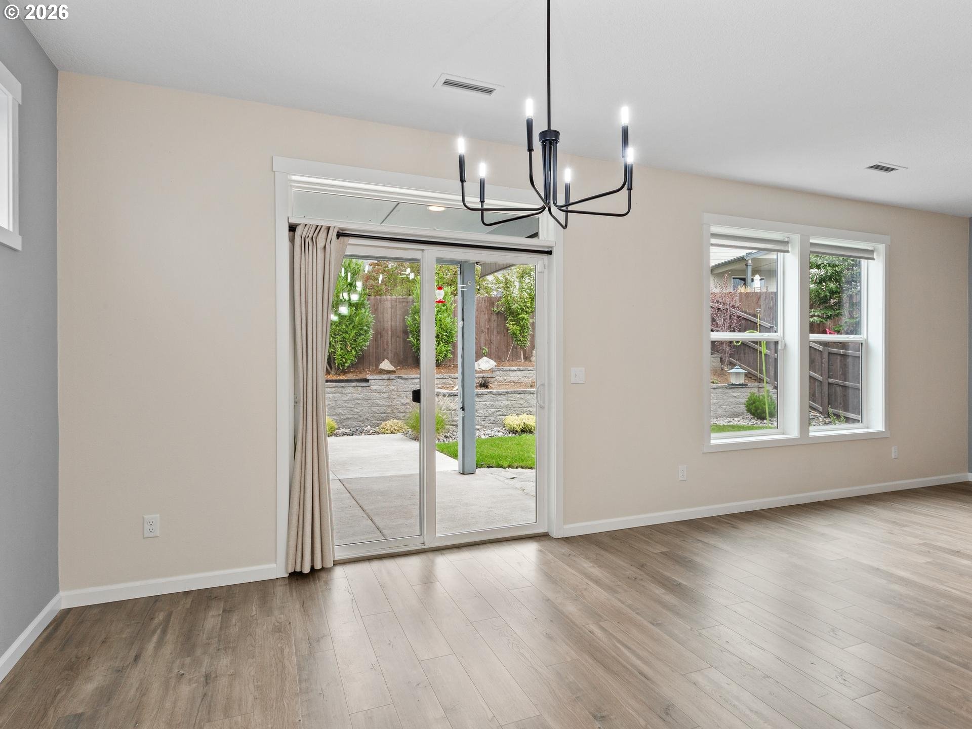 Empty dining area with a black chandelier, sliding glass door, and windows overlooking the yard.