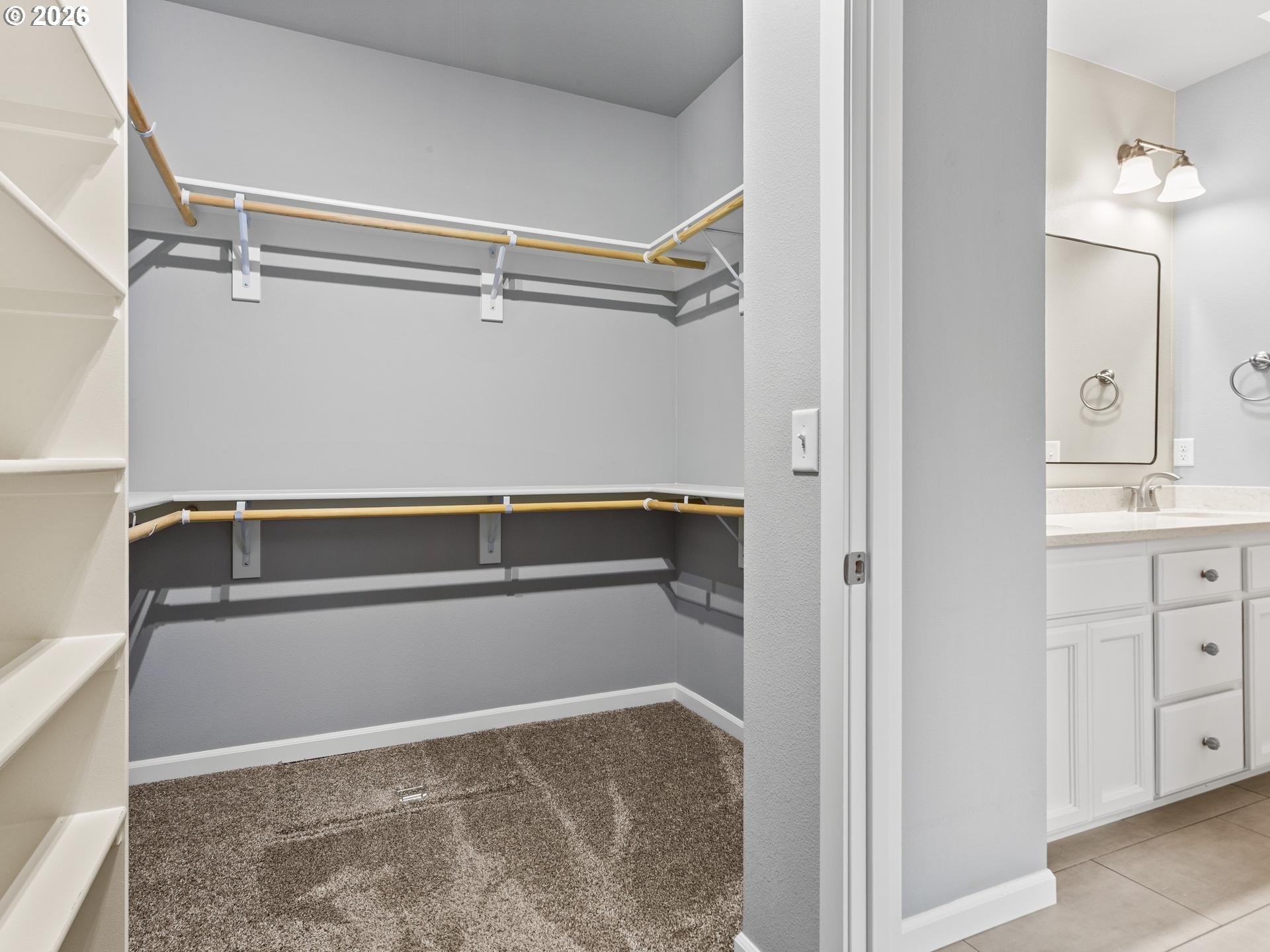 Walk-in closet with wraparound wooden hanging rods and built-in shelving beside a bathroom vanity.