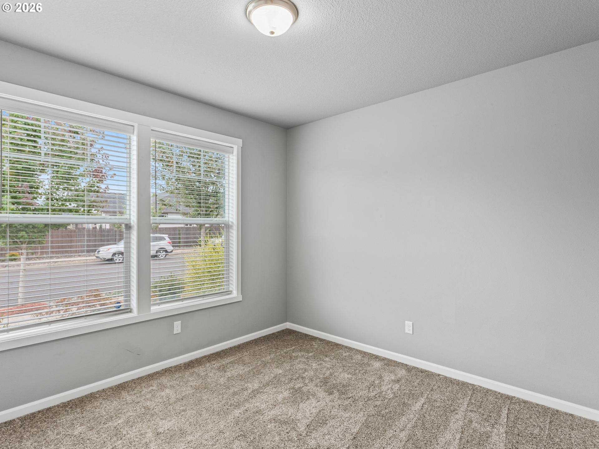 Empty bedroom with beige carpet and two large windows fitted with white blinds.