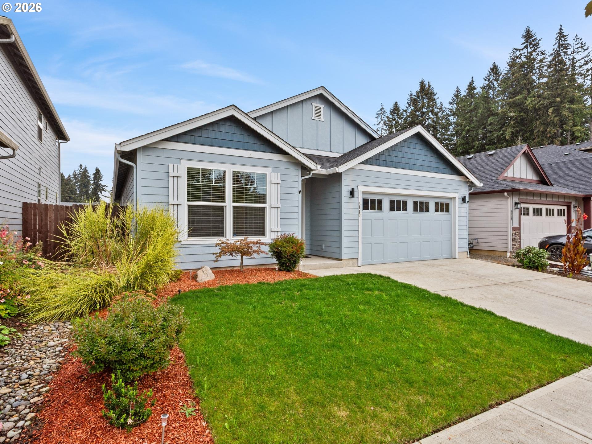 Blue-gray home with white trim, a two-car garage, and landscaped front lawn.