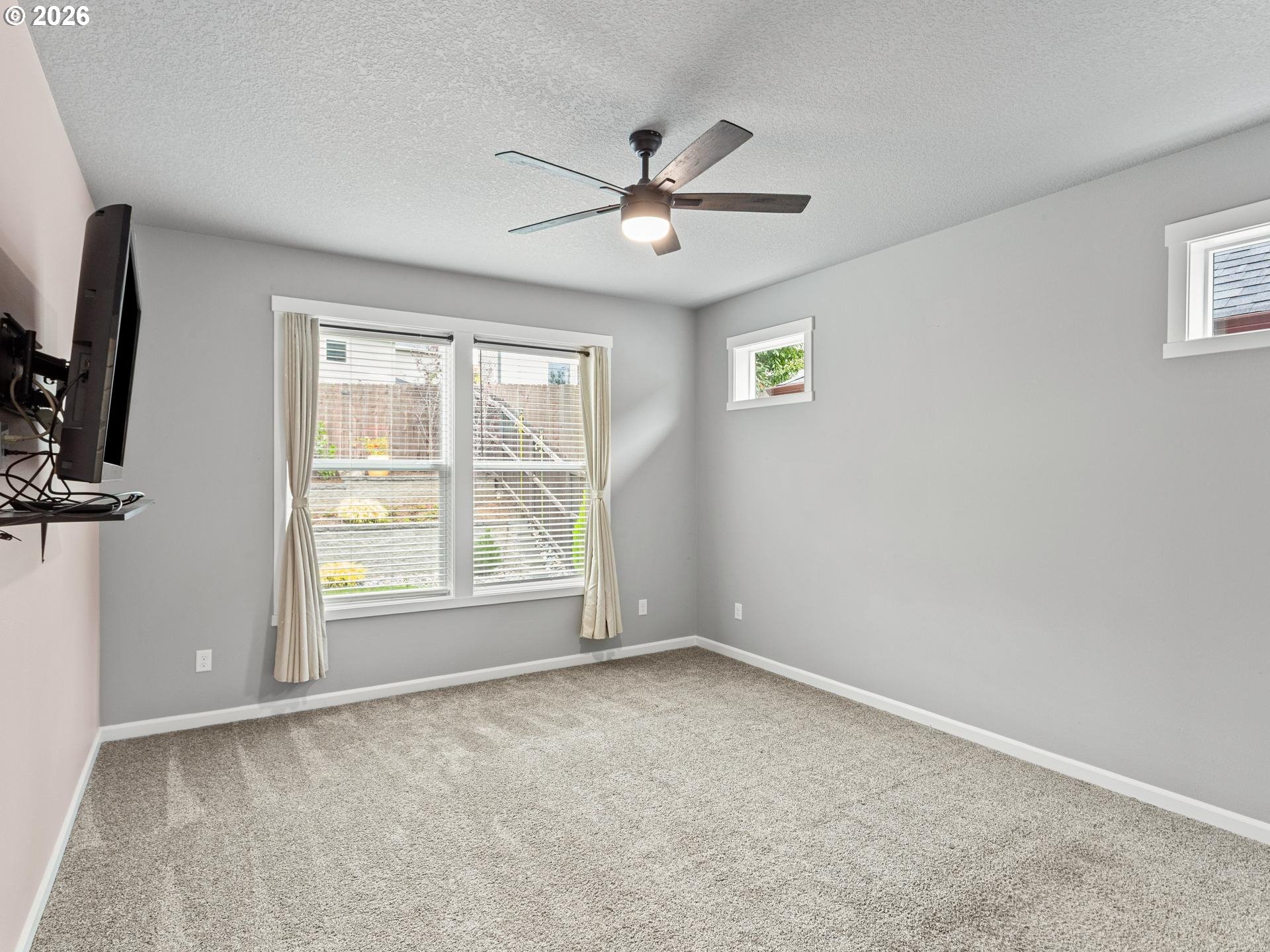 Empty carpeted bedroom with gray walls, a ceiling fan, and windows with blinds and curtains.
