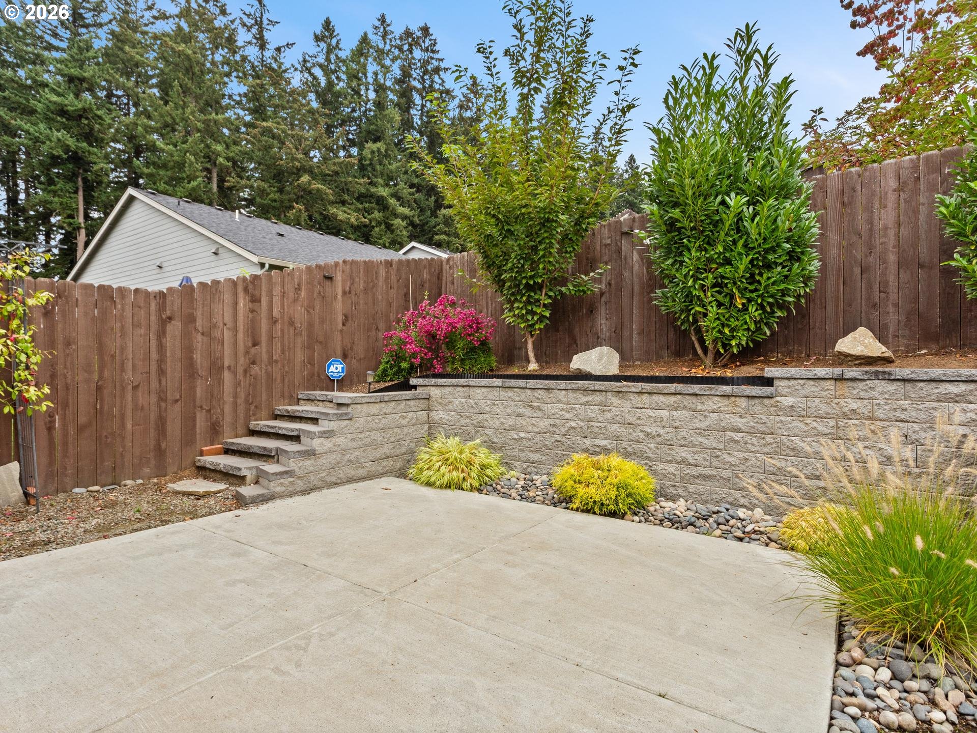 Backyard patio with stone retaining wall, steps, wooden privacy fence, and landscaped shrubs.
