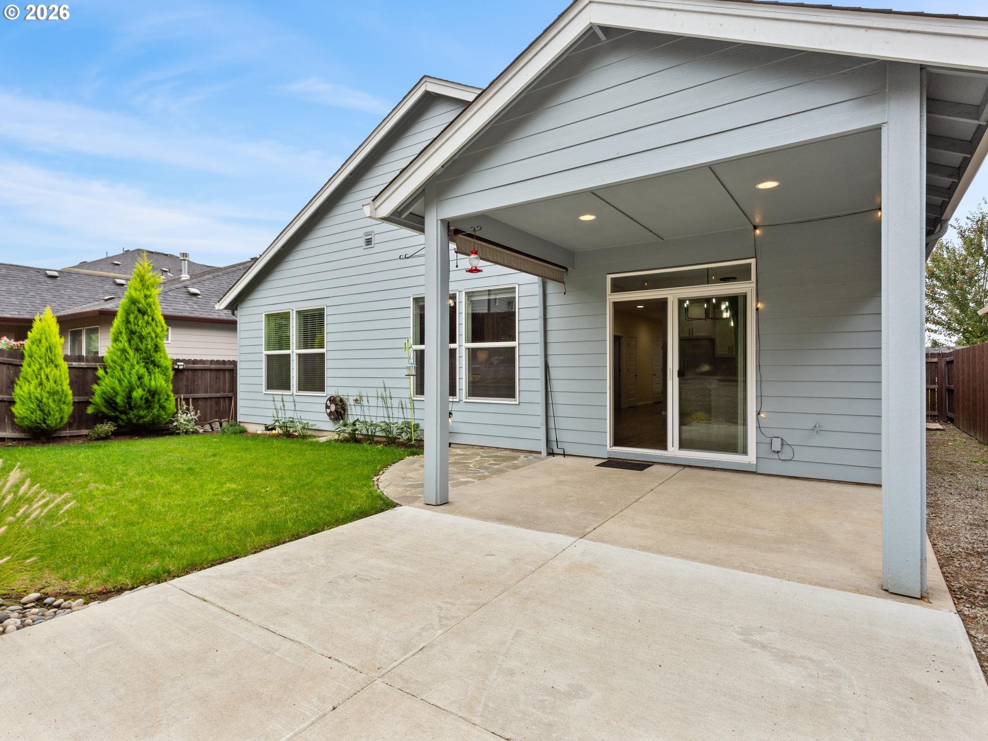 House with a covered concrete patio, sliding glass doors, and a fenced lawn.