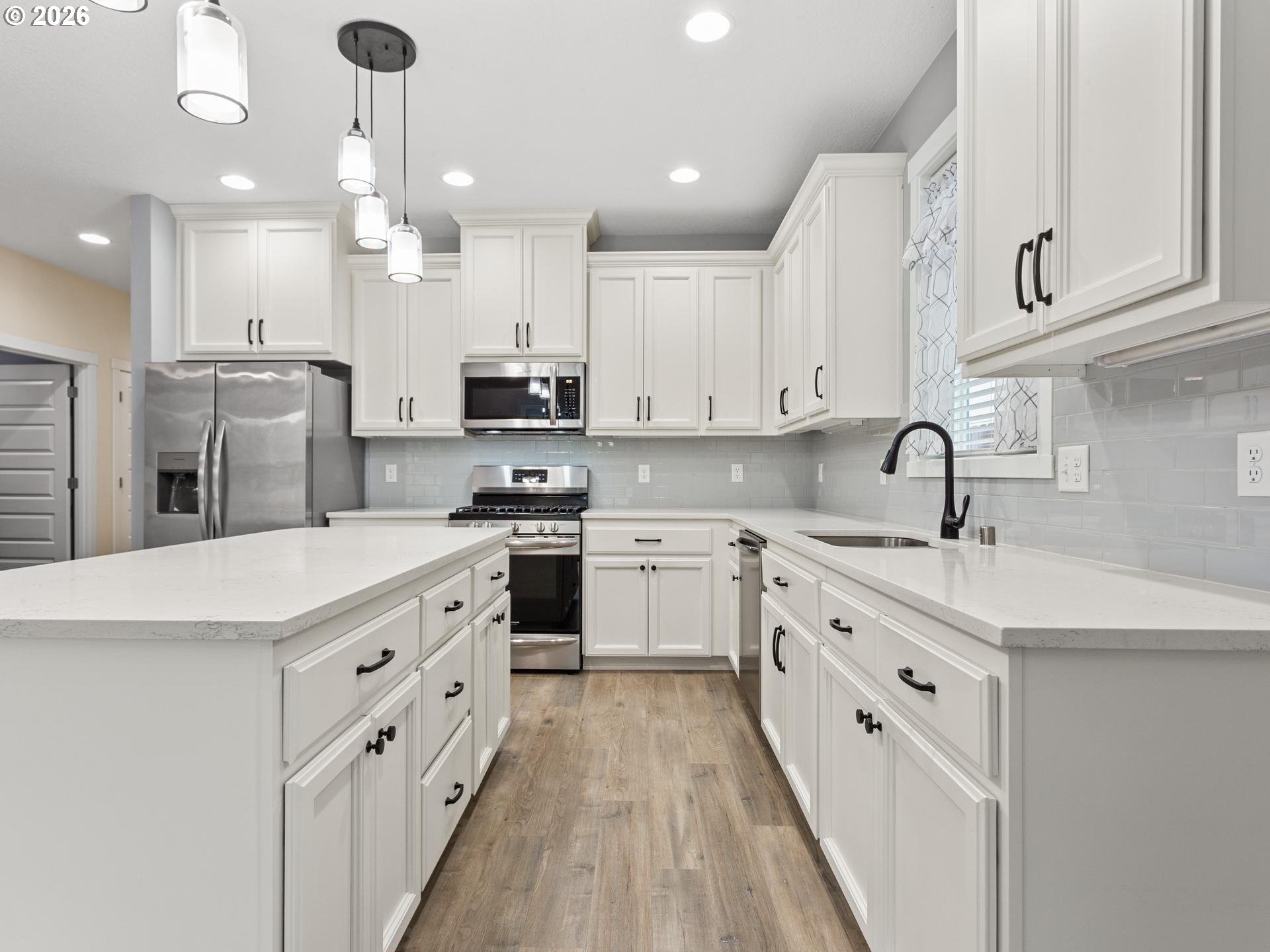 Bright white kitchen with a large island, quartz counters, stainless steel appliances, and wood-look flooring.