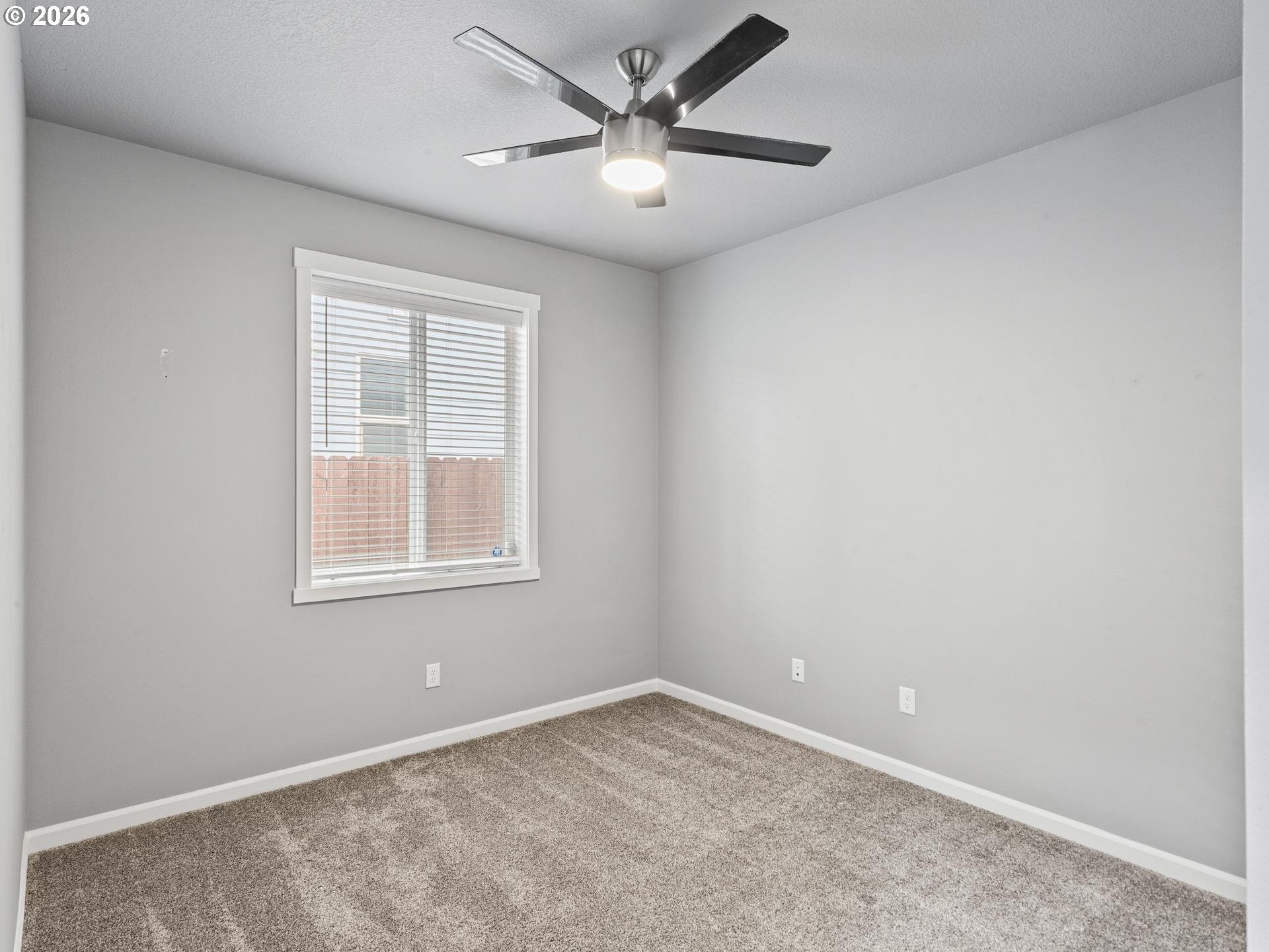 Empty bedroom with beige carpet, a window with white blinds, and a ceiling fan with light.
