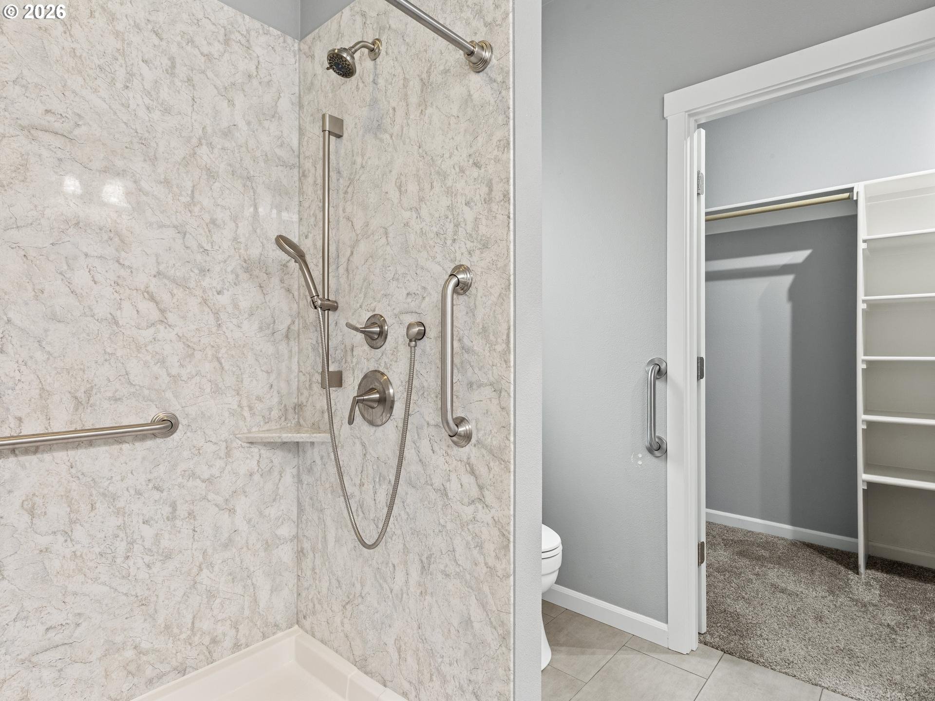 Bathroom with a marble-look walk-in shower, accessibility grab bars, and an adjoining walk-in closet.