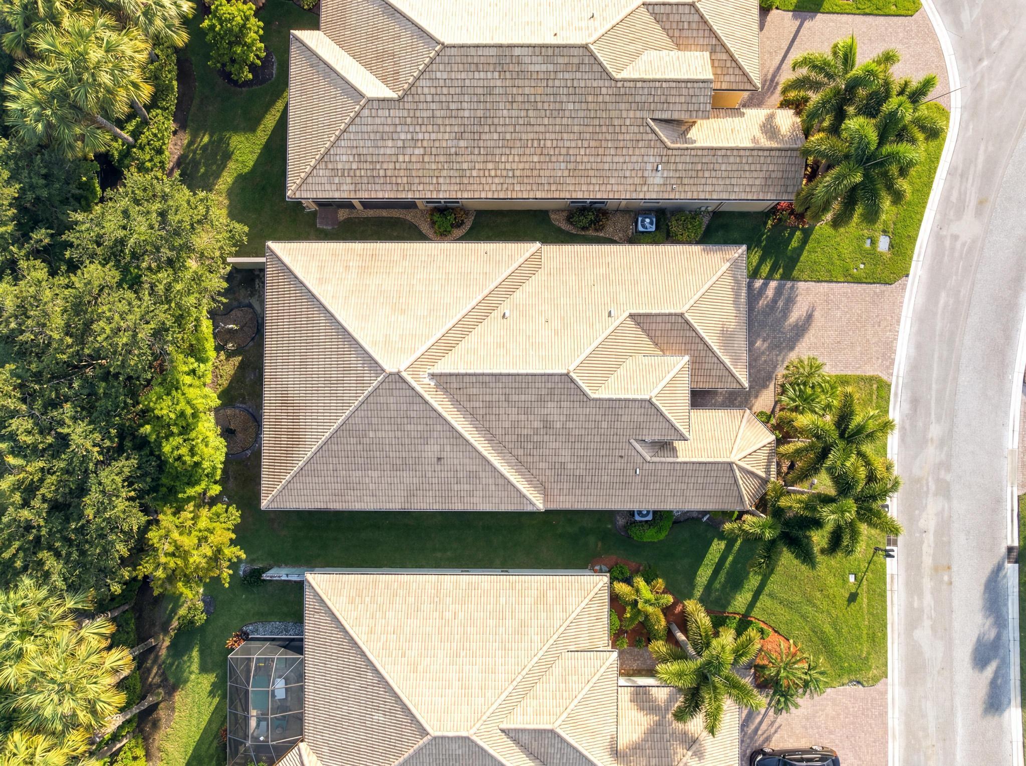 Aerial view of a tan tile-roofed home amid palms, lawns, and neighboring houses.