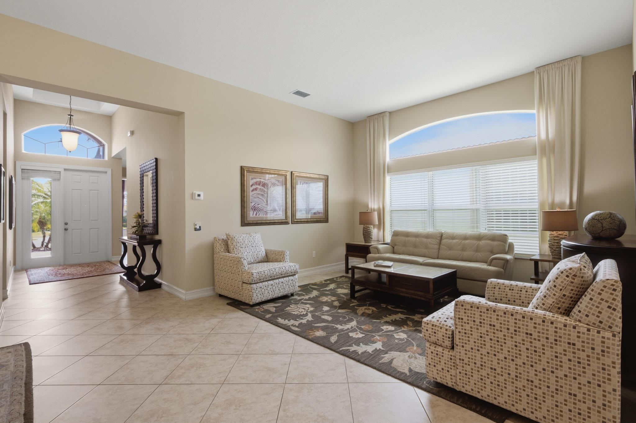 Furnished living room with beige seating, a floral rug, and a large arched window beside the entryway.