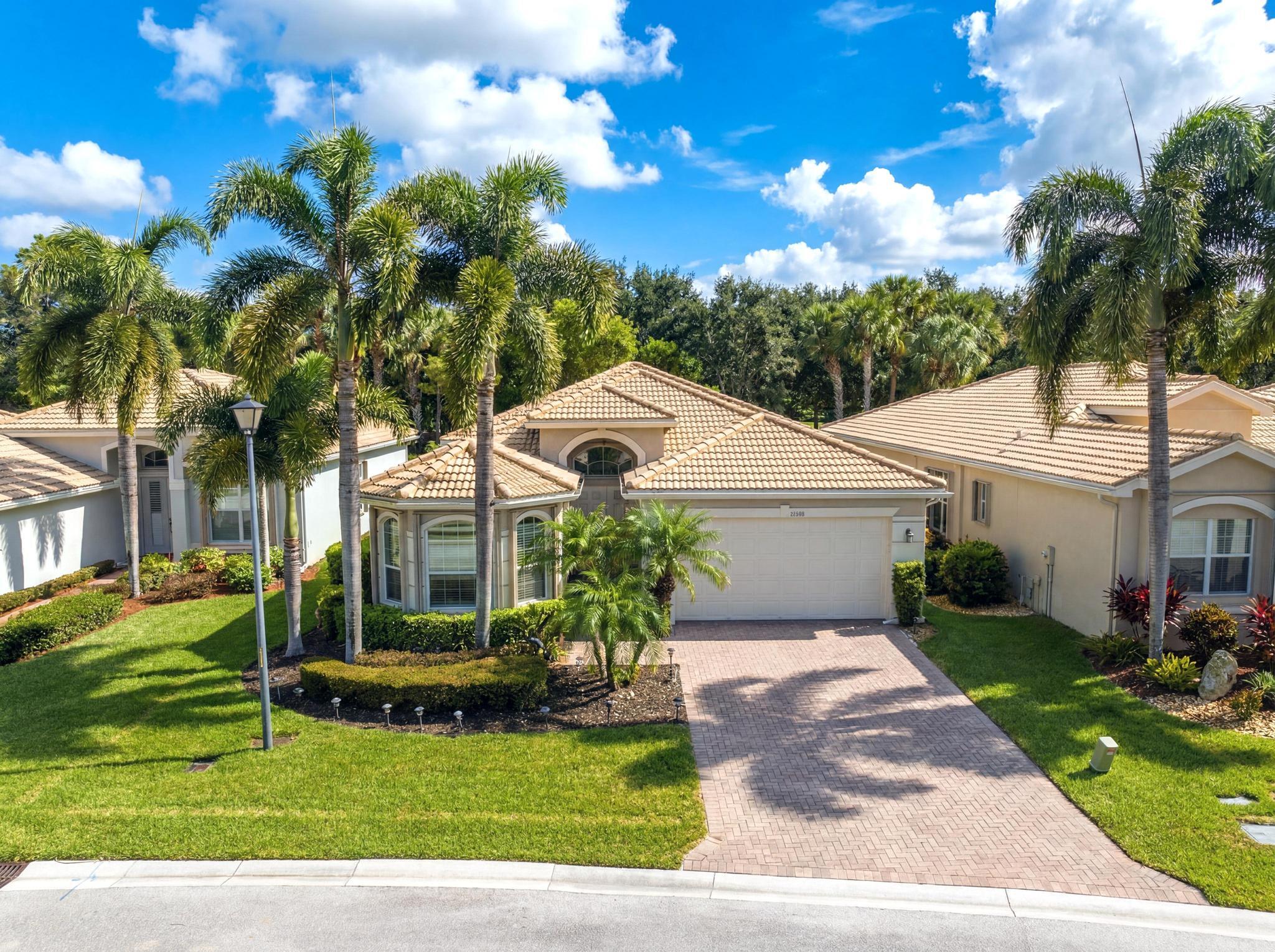 Single-story home with a tile roof, brick-paver driveway, and tall palm trees.