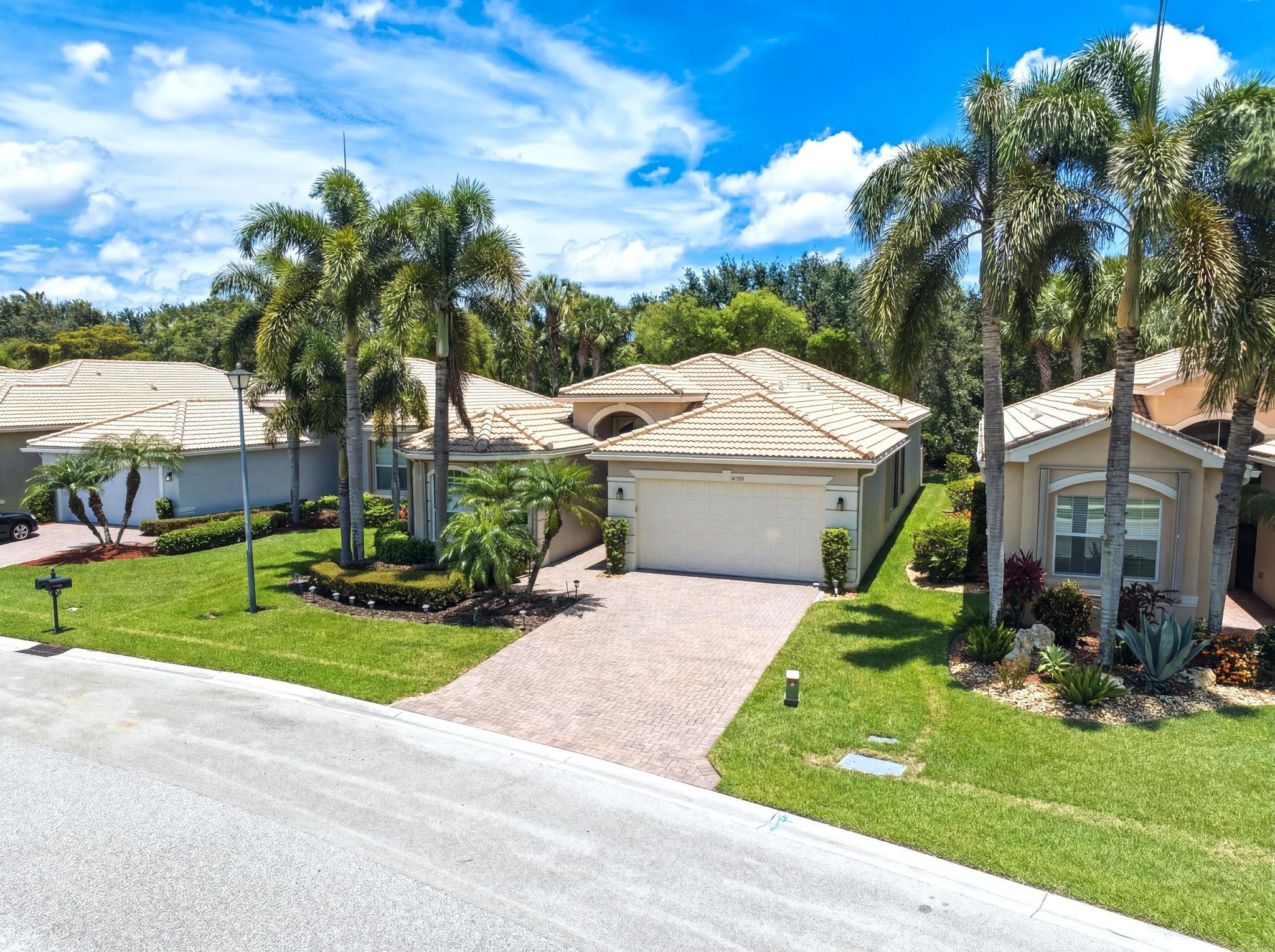 Single-story home with a tile roof, paver driveway, and palm-lined front yard.
