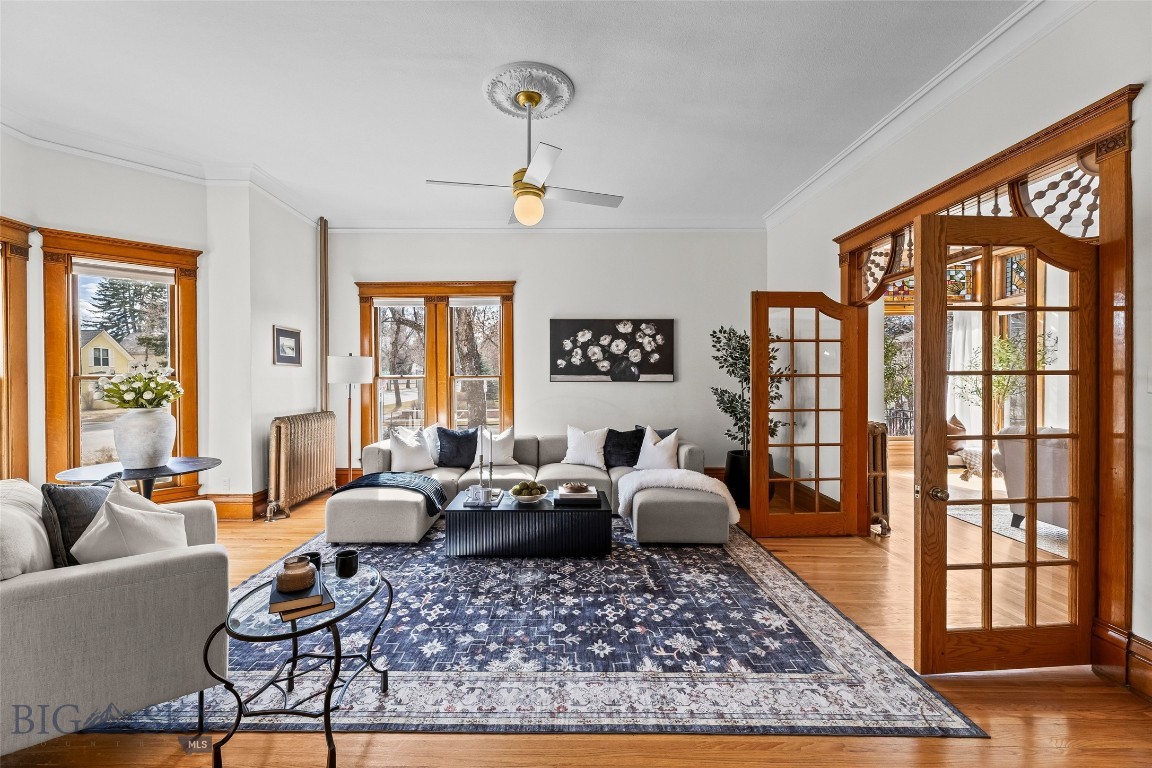 Staged living room with a large patterned rug, wood-trimmed windows, and open French doors.