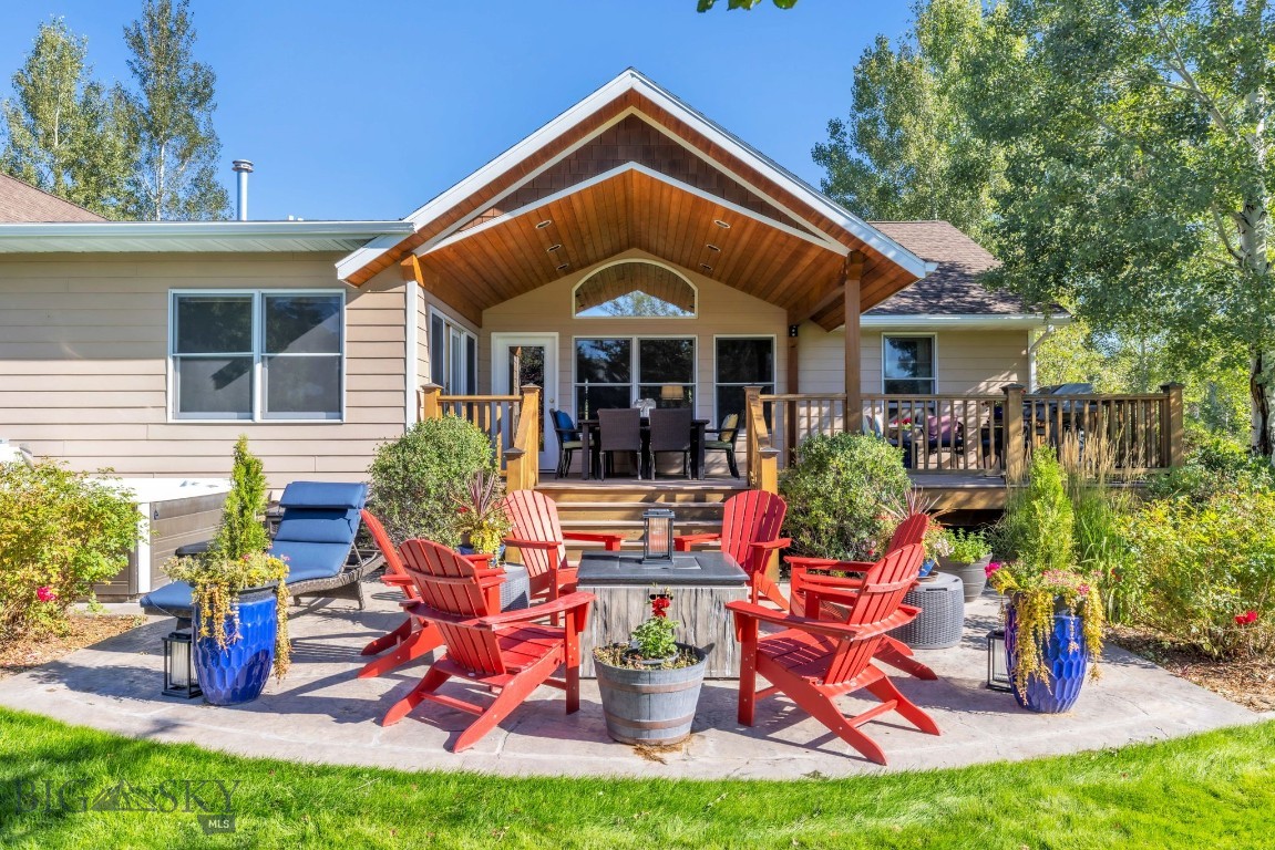 Home’s rear deck and patio with a timber gable, red Adirondack chairs, and fire table.