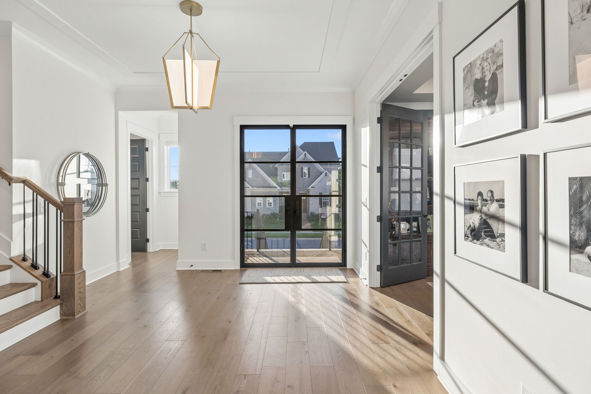 Entry foyer with wood floors, a black-framed glass front door, staircase, and framed photographs.