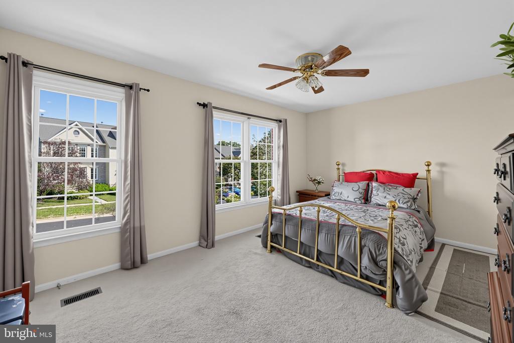 Bedroom with a brass bed, gray patterned bedding, red pillows, and two large windows.