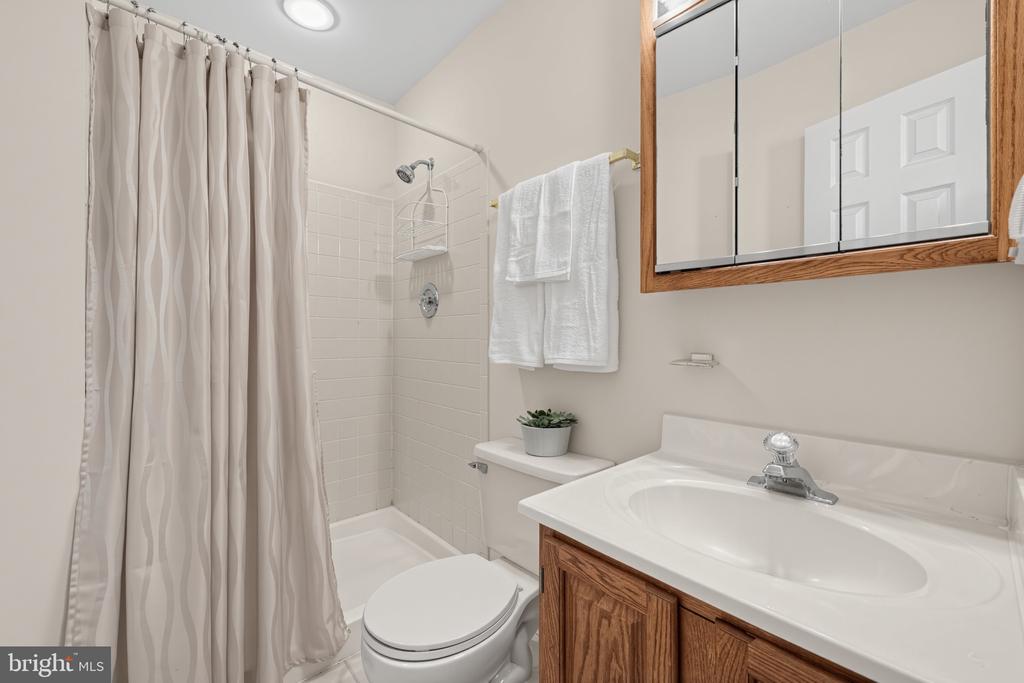 Bathroom with a tiled shower, patterned curtain, and wood vanity.