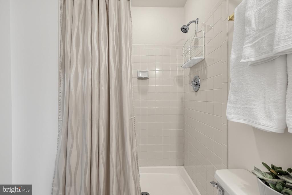 Bathroom tub and shower with white tile, striped curtain, chrome fixtures, and white towels.