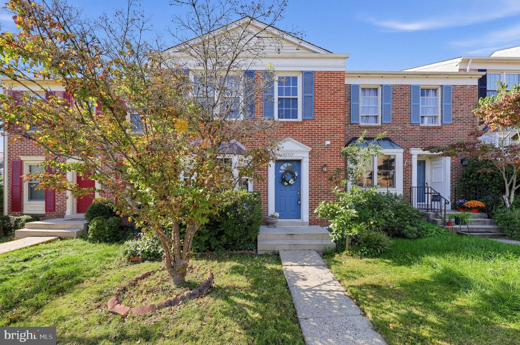 Brick townhouse with a blue front door, white trim, and a leafy front yard.
