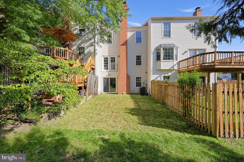 Rear of a light-sided home with a brick chimney, wooden decks, and a fenced grassy yard.
