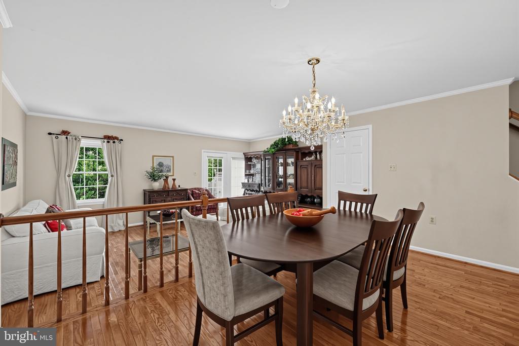 Dining room with a crystal chandelier, dark wood table, and hardwood floors adjoining a living area.