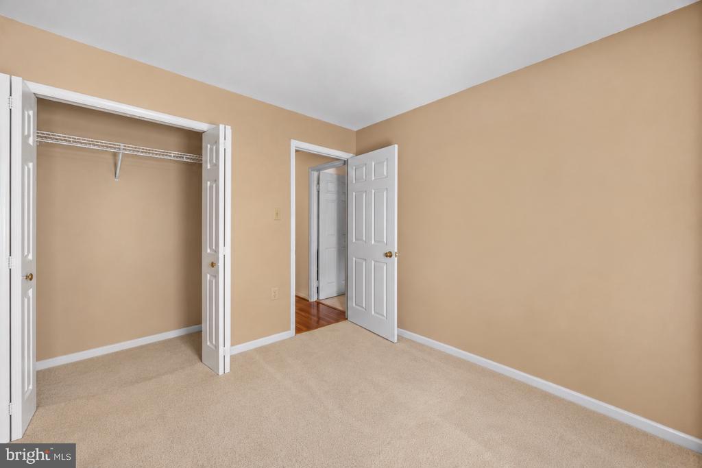 Unfurnished bedroom with beige carpet, an open closet, and a doorway to a hardwood-floored hall.