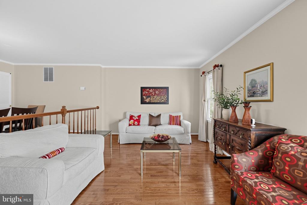 Living room with hardwood floors, white sofas, a patterned accent chair, and dark wood dresser.