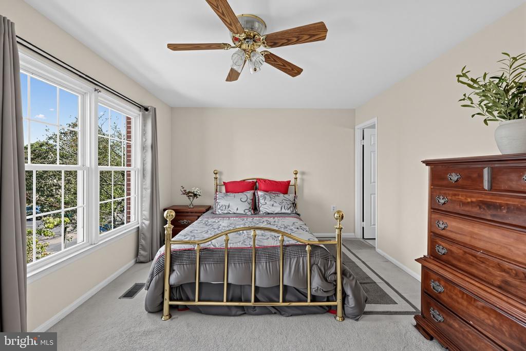 Bedroom with a brass bed, red accent pillows, tall windows, and a wooden dresser.