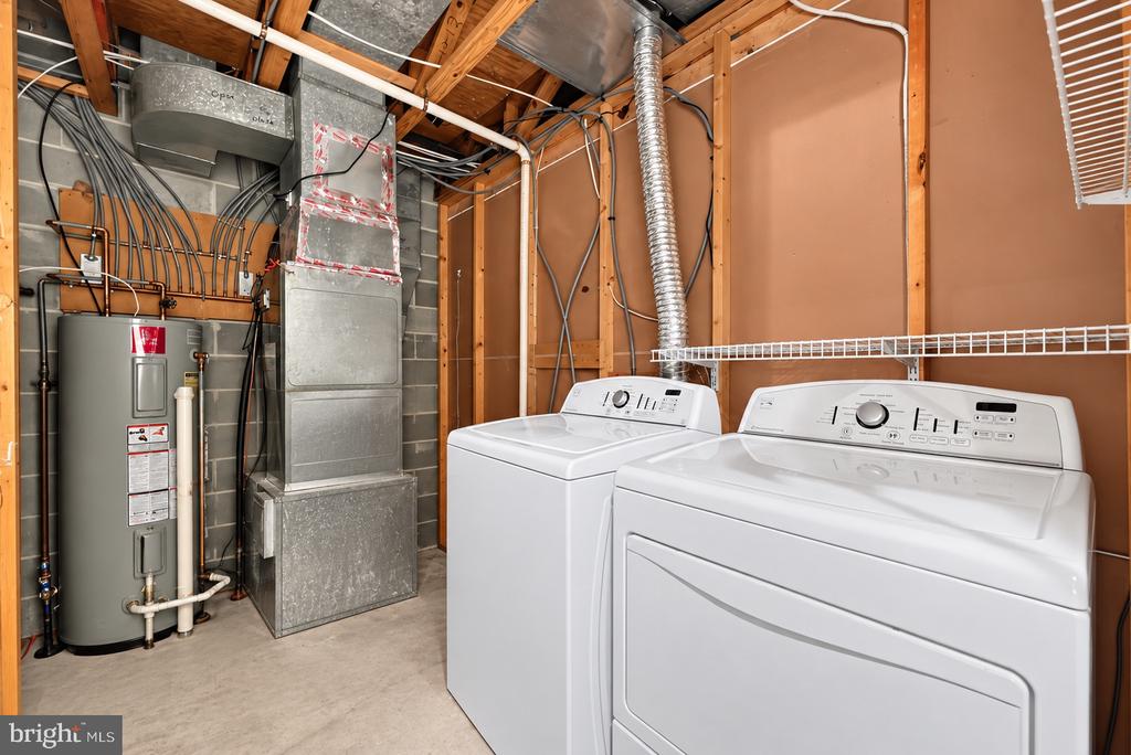 Laundry area with white washer and dryer beside the water heater and exposed HVAC ductwork.