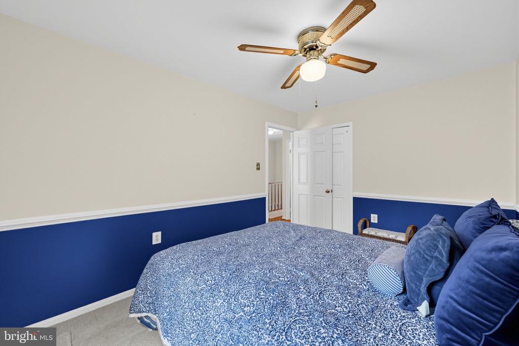 Bedroom with blue patterned bedding, two-tone walls, and a ceiling fan.