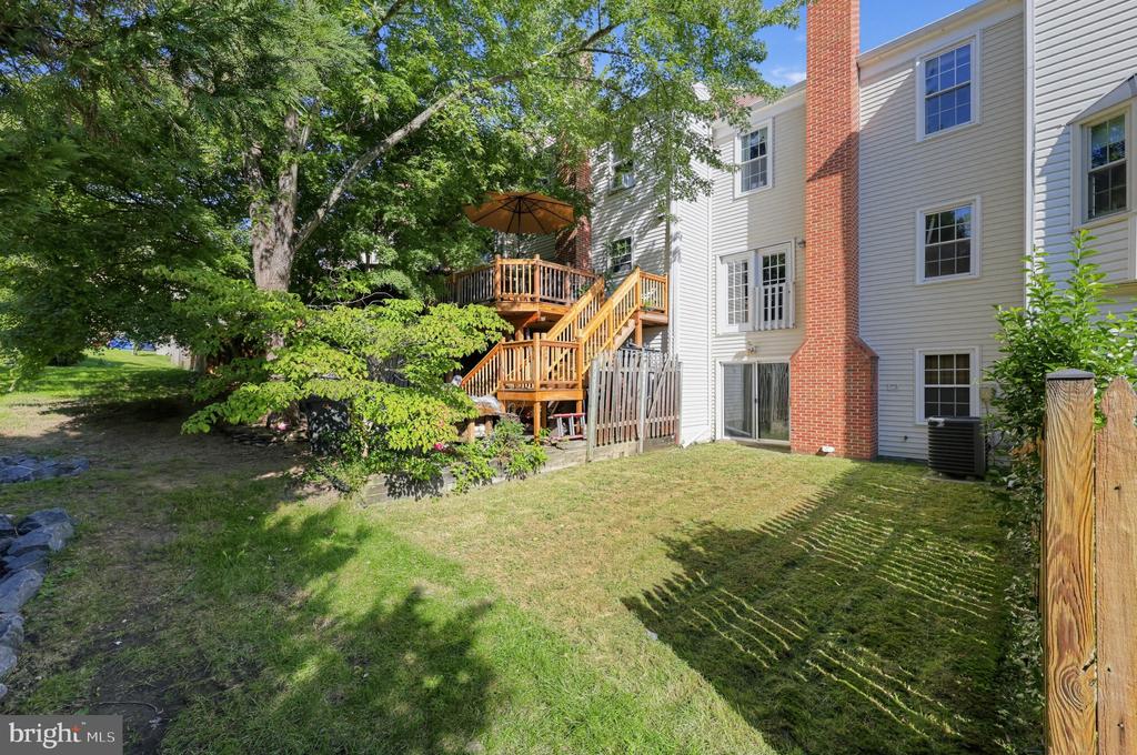 Townhouse rear exterior with a raised wooden deck, brick chimney, and tree-shaded yard.