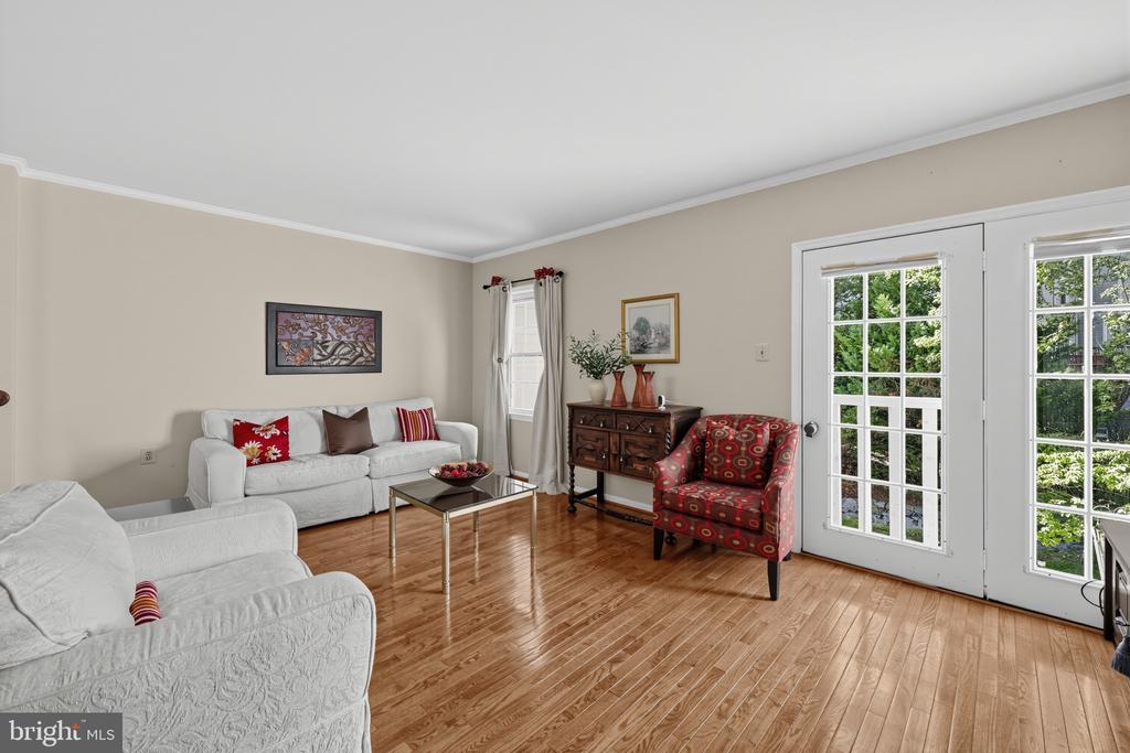 Living room with white sofas, a patterned red armchair, hardwood floors, and glass-paneled French doors.