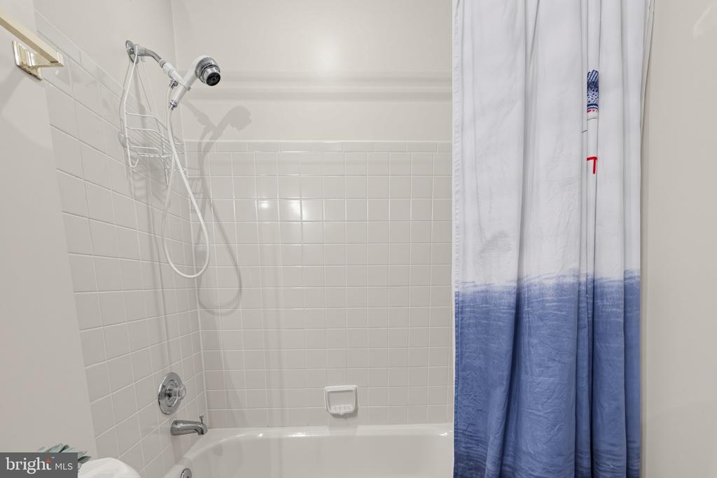 Bathroom tub and tiled shower with a handheld showerhead and blue-and-white curtain.