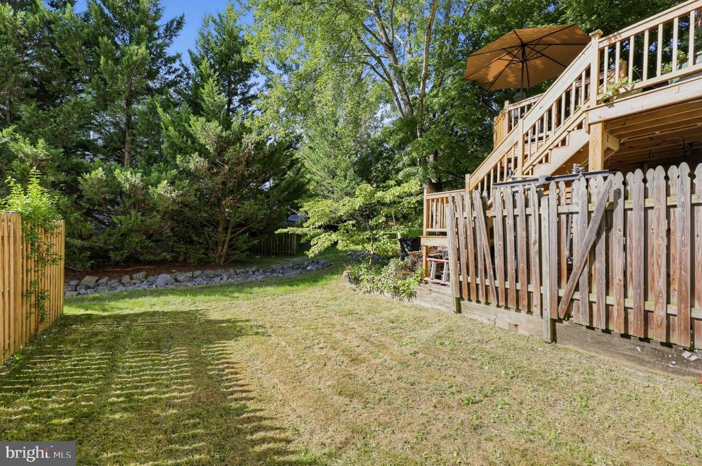 Backyard with a raised wooden deck, tan umbrella, lawn, and mature trees.