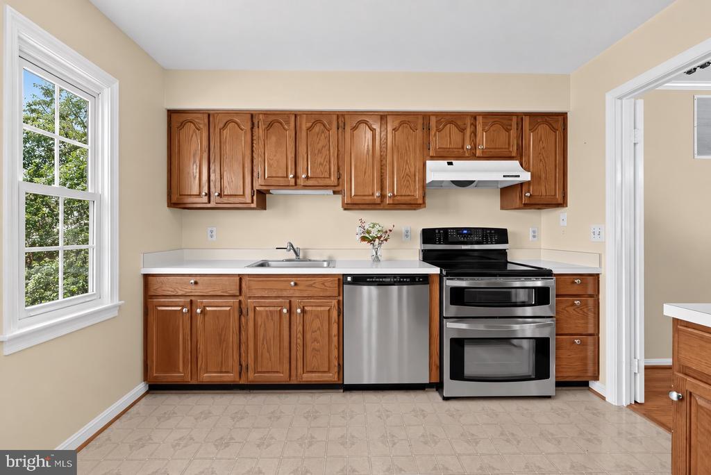 Kitchen with warm wood cabinets, stainless steel appliances, and a large window overlooking trees.