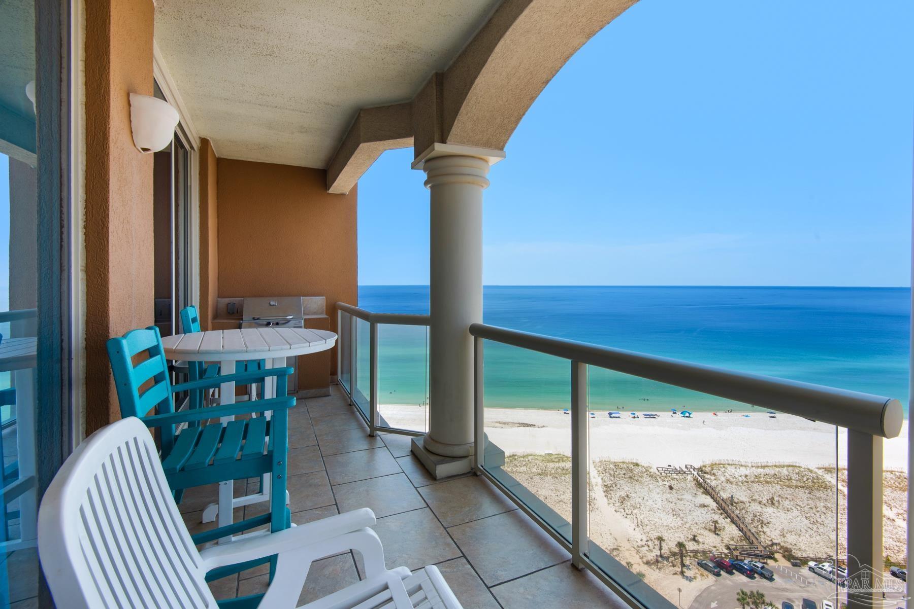 Condo balcony overlooking the beach and Gulf, furnished with turquoise chairs and a small table.