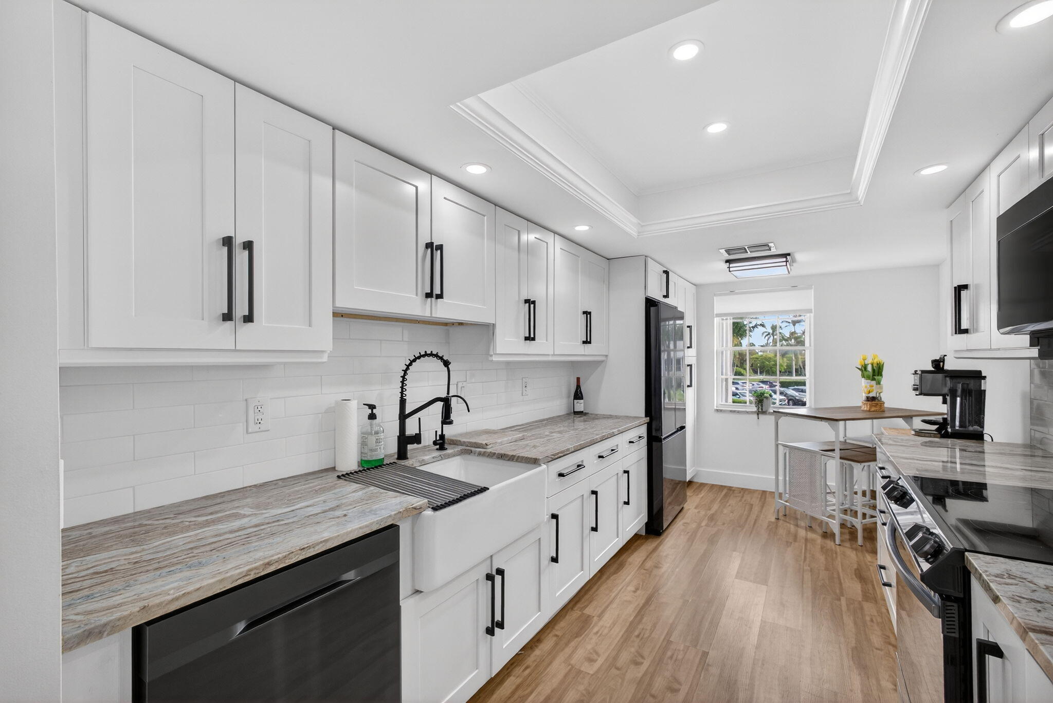 Renovated kitchen with white cabinets, veined countertops, farmhouse sink, and dining table by a window.