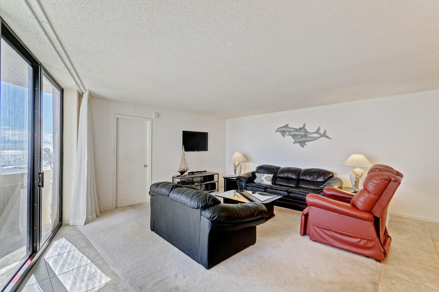 Living room with black leather sofas, a red recliner, and ocean views through sliding glass doors.
