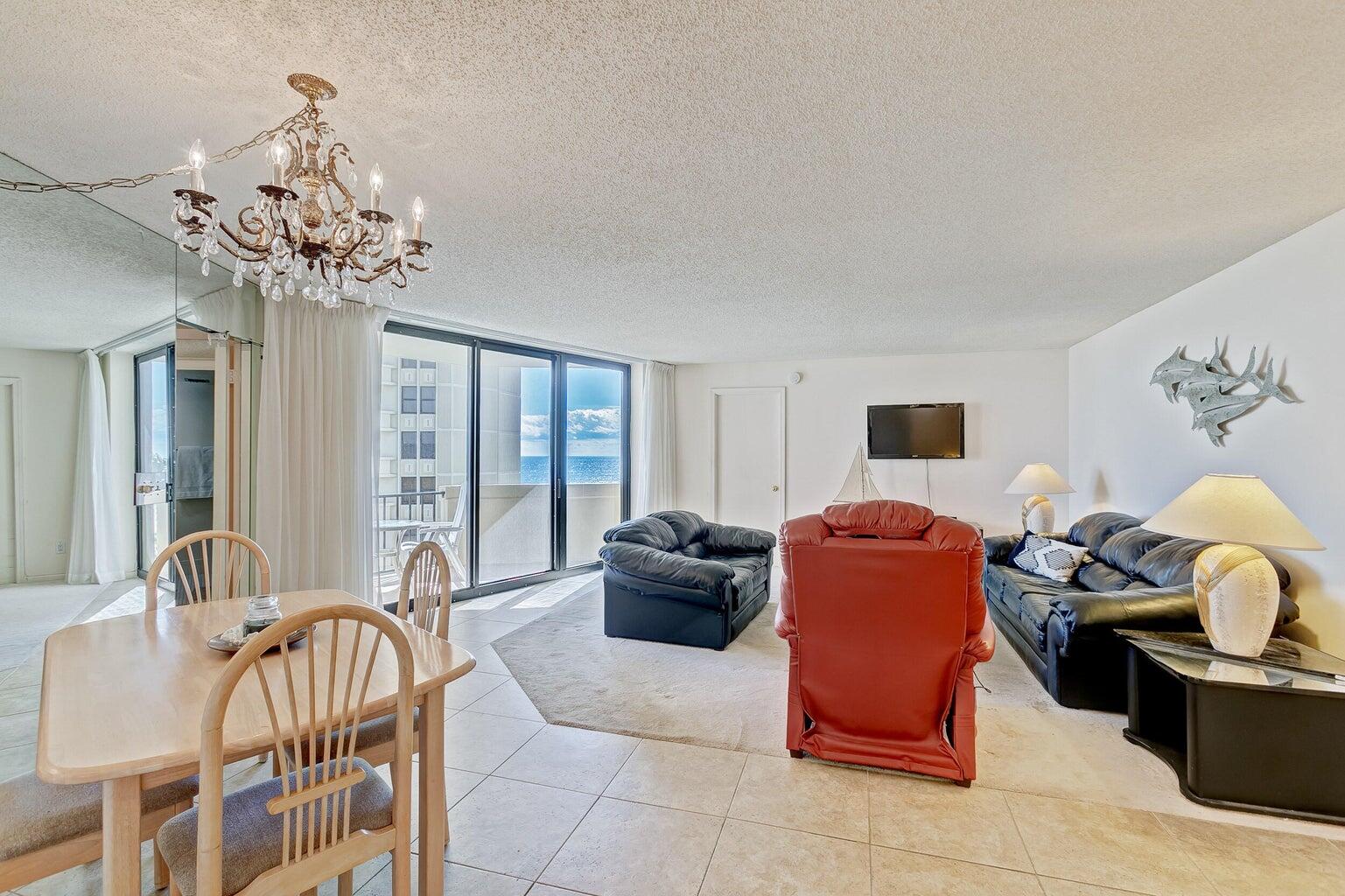 Furnished condo living and dining area with leather seating and ocean views through sliding glass doors.
