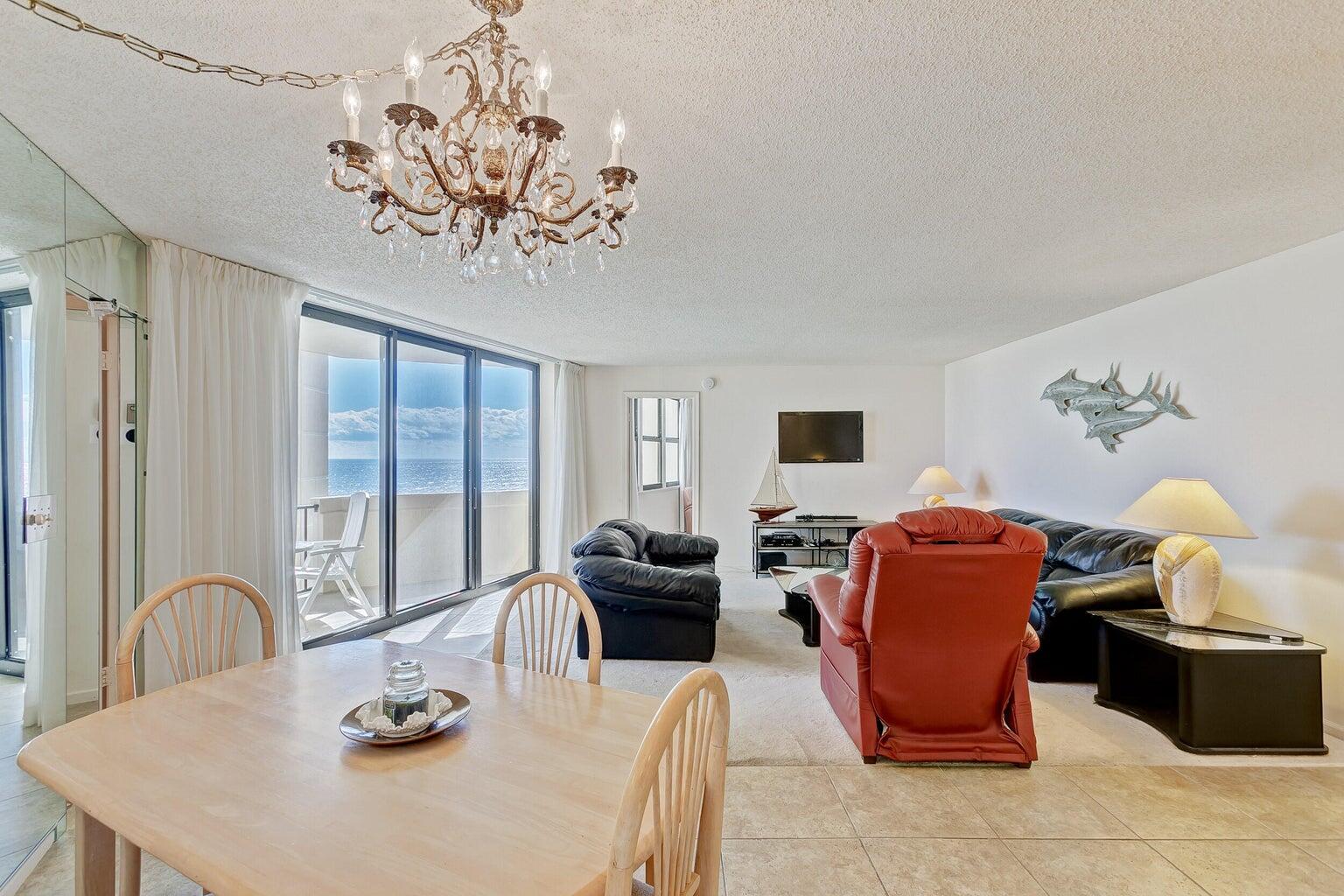 Furnished condo living and dining area with ocean views through sliding glass doors and a chandelier.