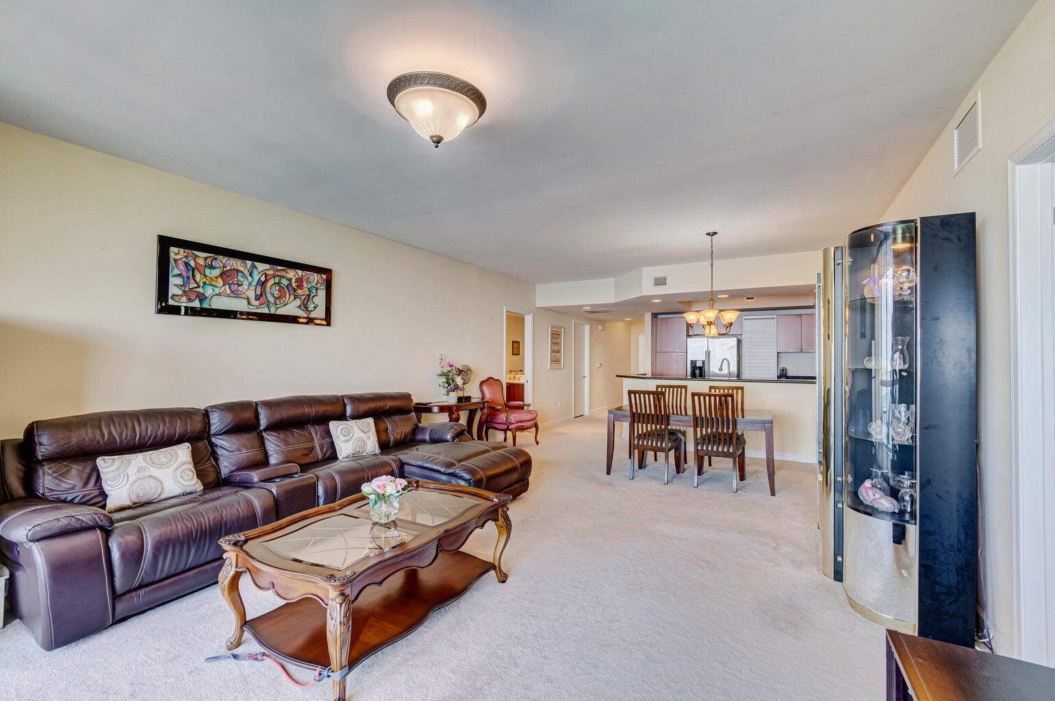 Condo living and dining area with a leather sectional, glass coffee table, and open kitchen.