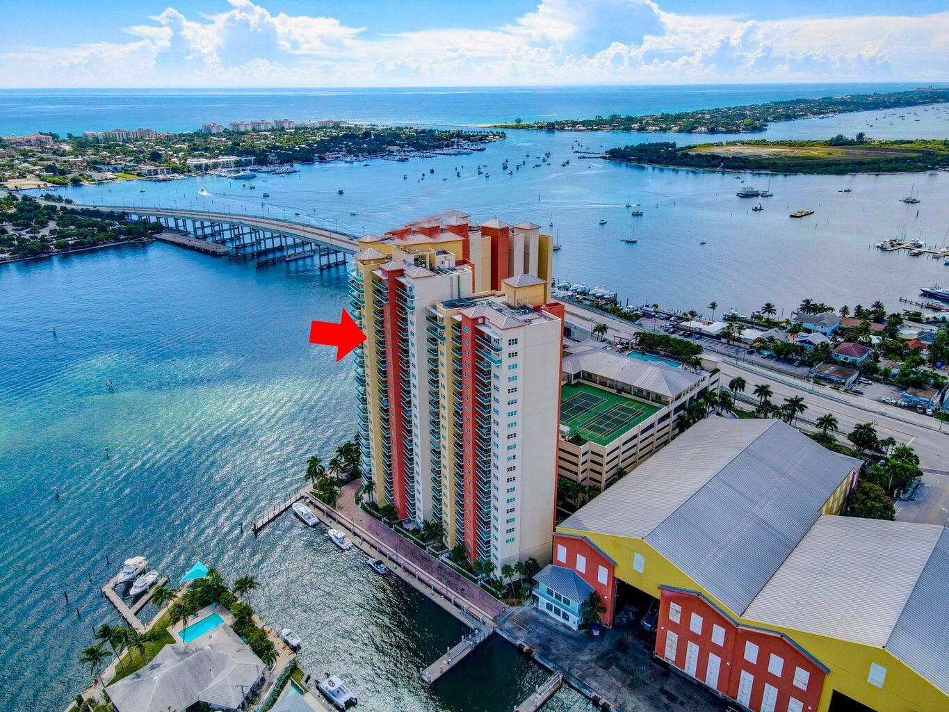 Waterfront condominium tower marked by a red arrow, beside a marina and broad waterway.