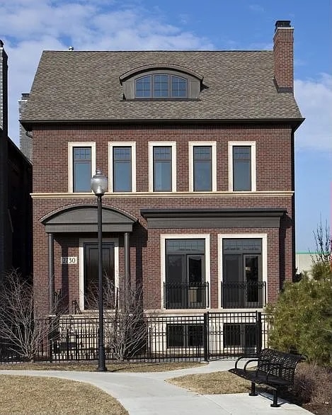 Red-brick home with an arched entry, gray shingle roof, and black metal fence.