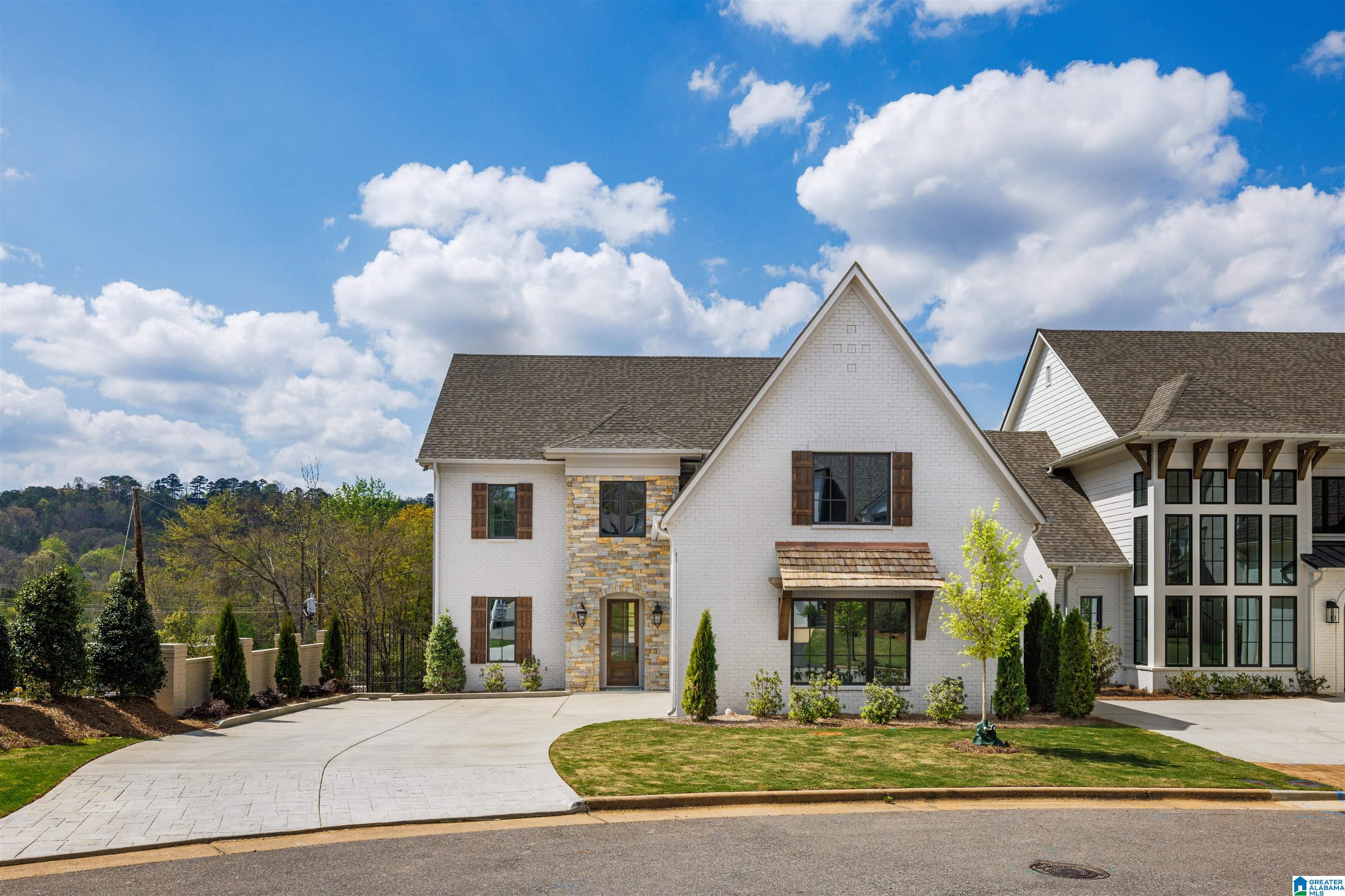 White-brick two-story home with stone accents, dark shutters, and a broad curved driveway.