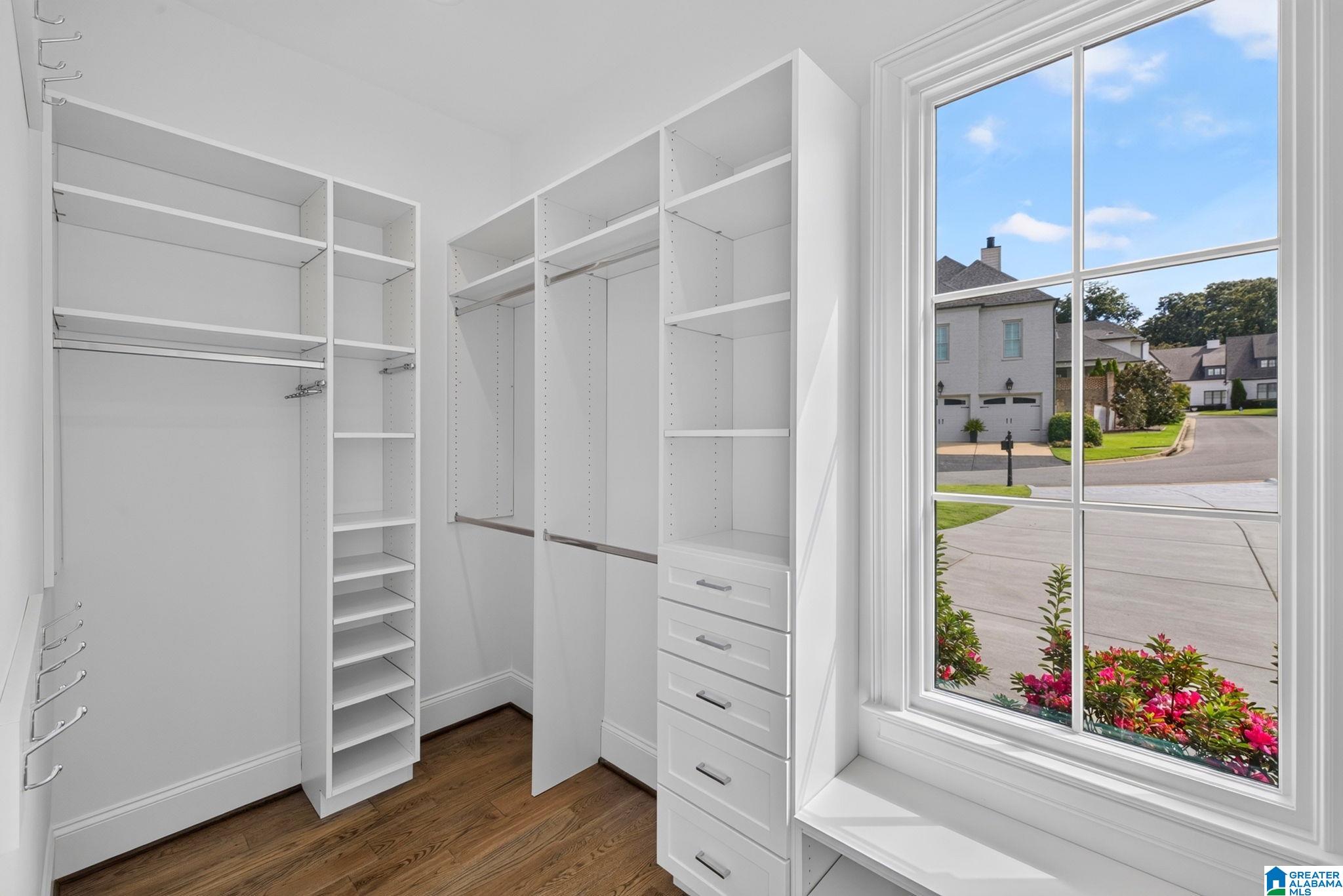 Walk-in closet with white built-in shelving and drawers beside a large street-facing window.