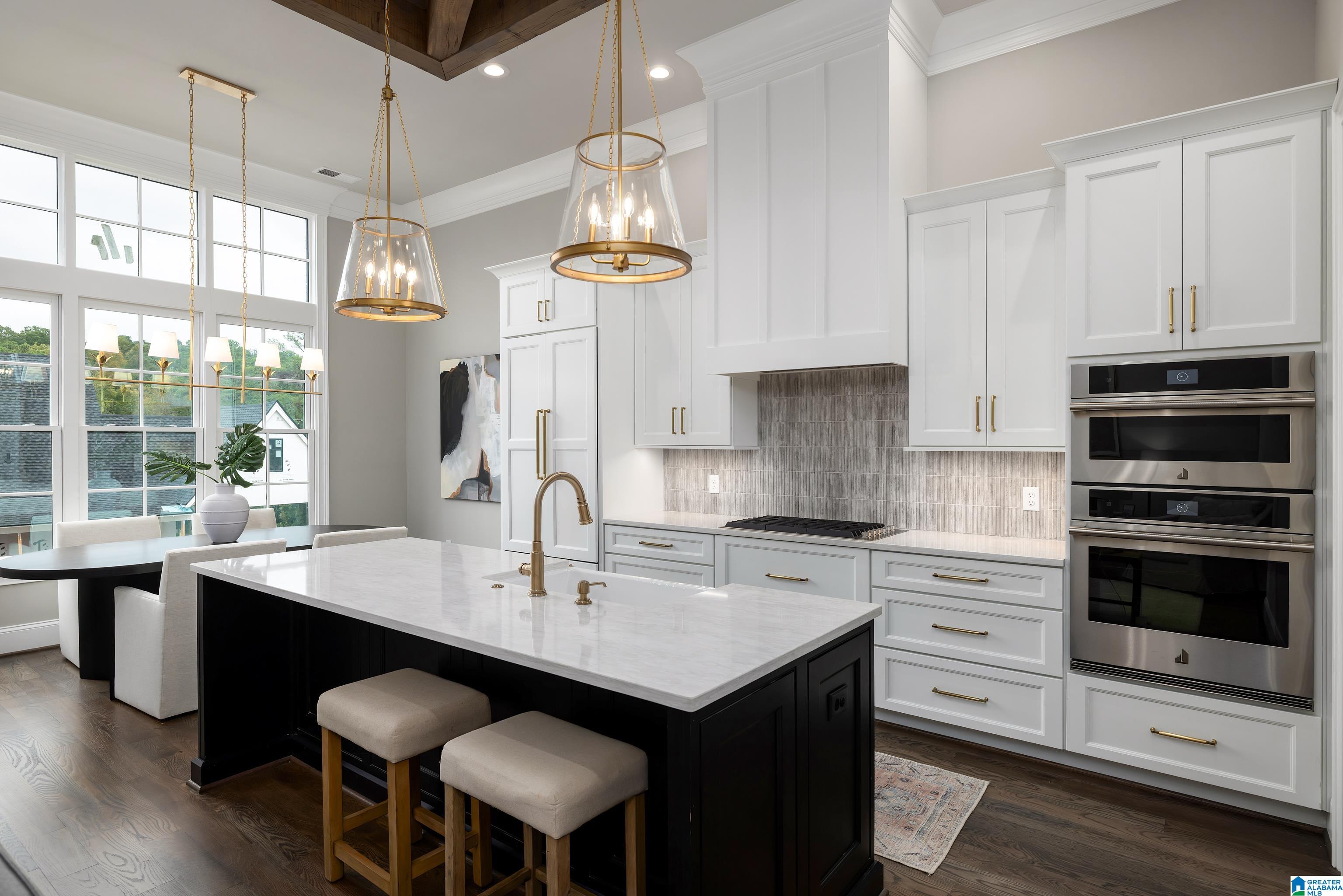 Bright kitchen with a marble-topped black island, white cabinets, brass pendants, and stainless steel double ovens.