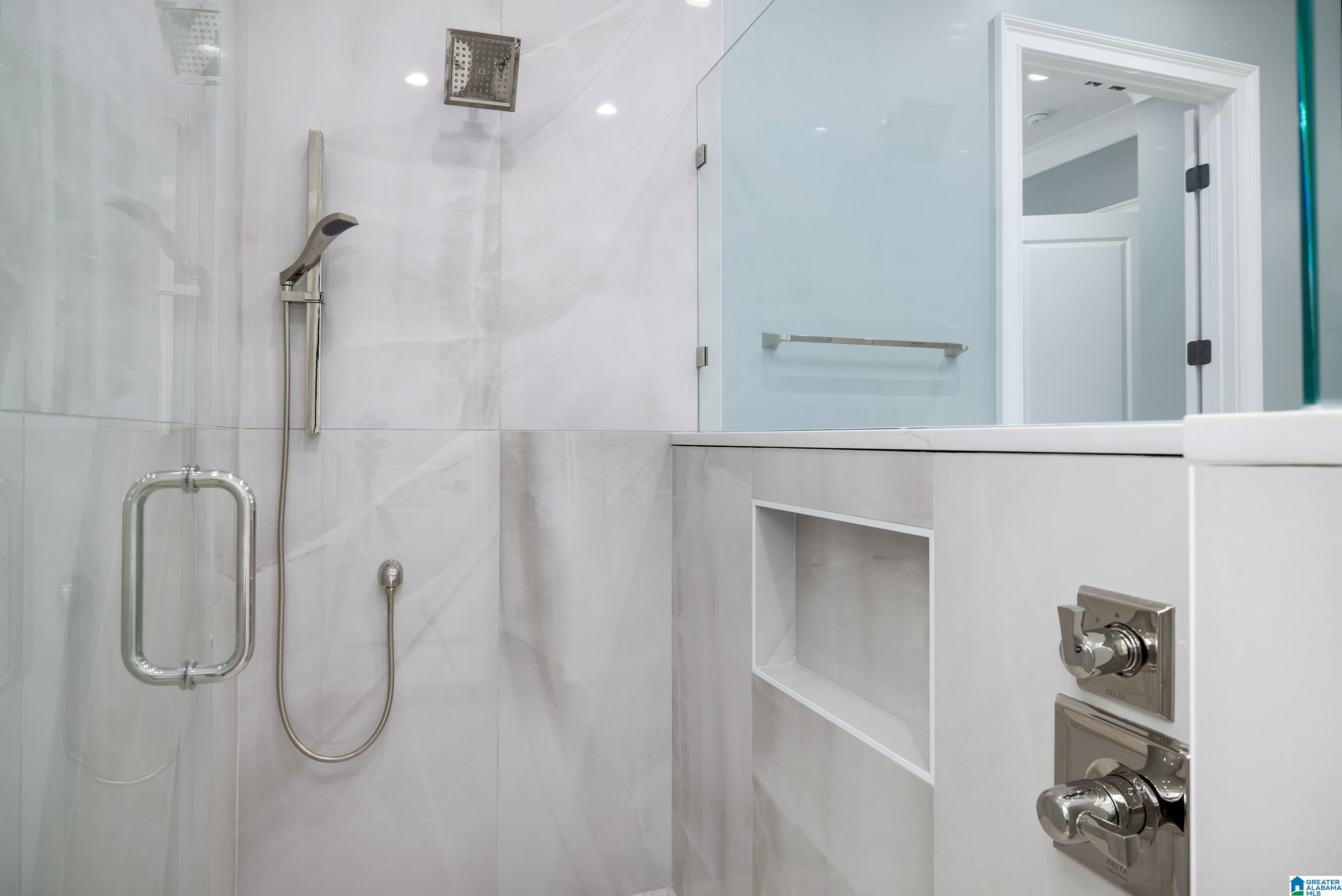 Modern tiled shower with frameless glass, rain showerhead, handheld sprayer, and recessed wall niche.
